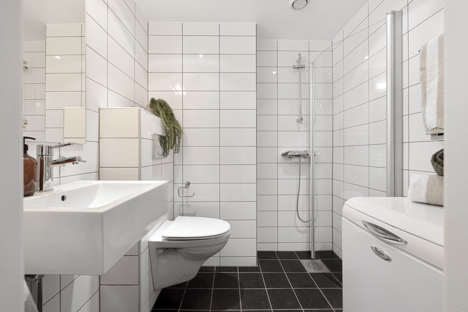 Flislagt bad med servant, toalett, opplegg til vaskemaskin og dusjhjørne med glassdør Galleribilde