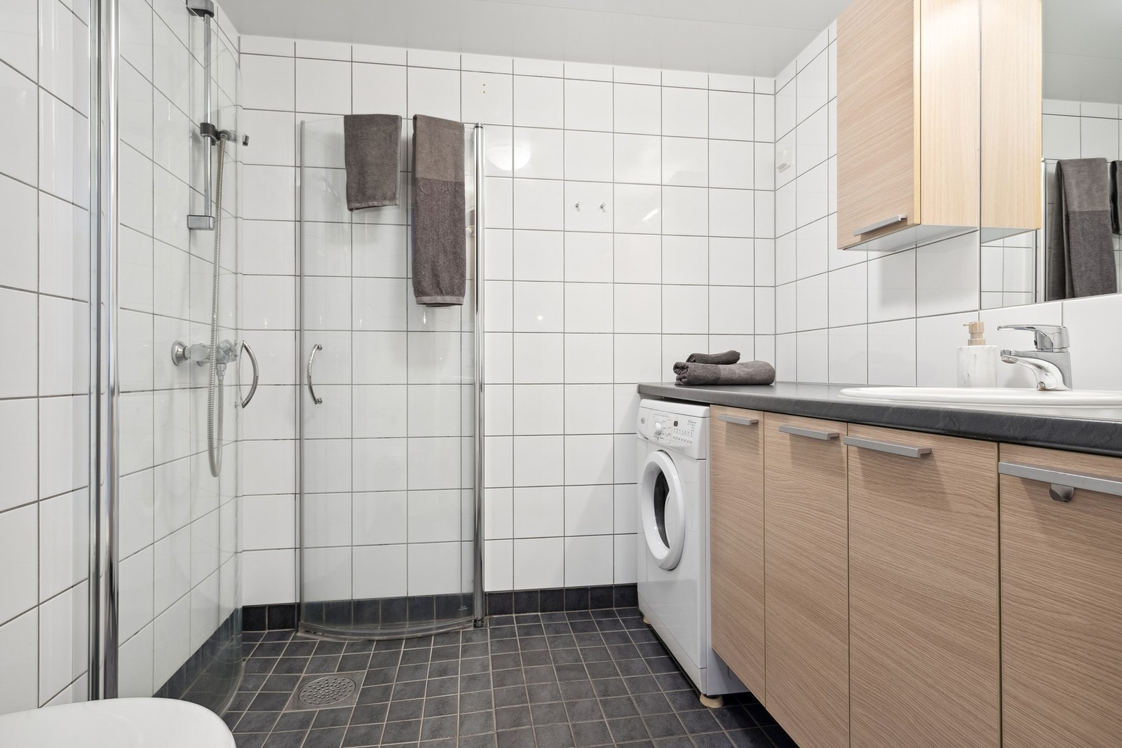 Et flott flislagt bad på 4 kvm, med varmekabler i gulv. Badet er utstyrt med plassbesparende dusjvegger i glass samt kran/avløp for vaskemaskin. Galleribilde