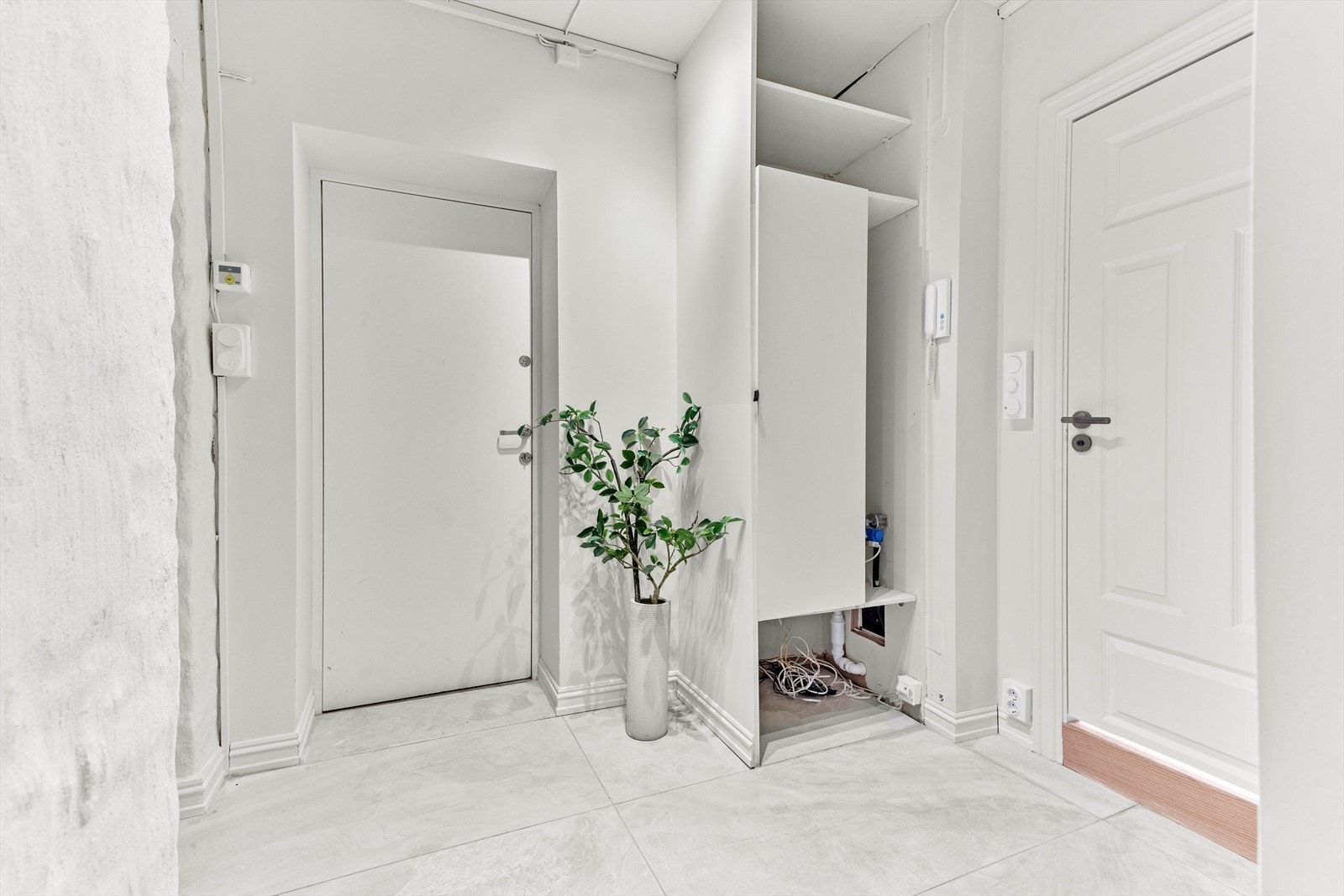 Velkommen inn! Ytterklær henges og sko plasseres i en fin plassbygget garderobeløsning m/ opplegg for vaskemaskin. Det er også plass til oppbevaringsløsninger langs den andre veggen.
60 x 60 fliser på gulv med varmefolie. Galleribilde