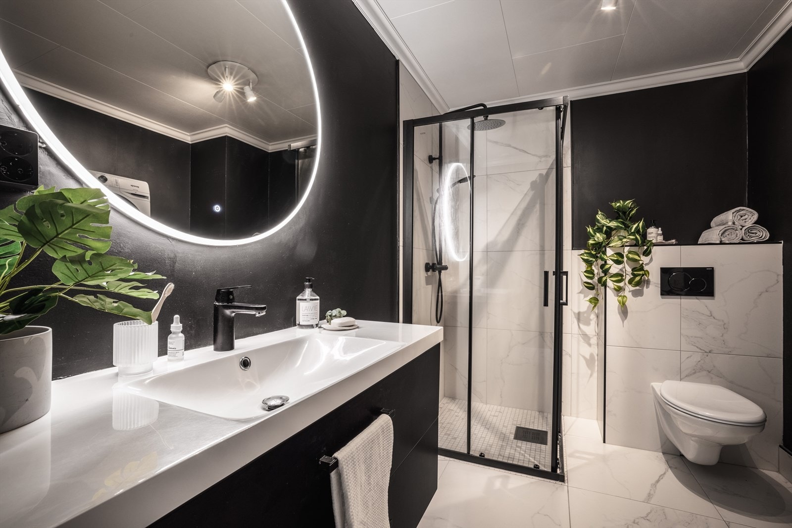 Badet er utstyrt med vegghengt toalett, servantmøbler og dusjhjørne. Flotte fliser med marmoruttrykk med nydelige svarte kontraster. Galleribilde