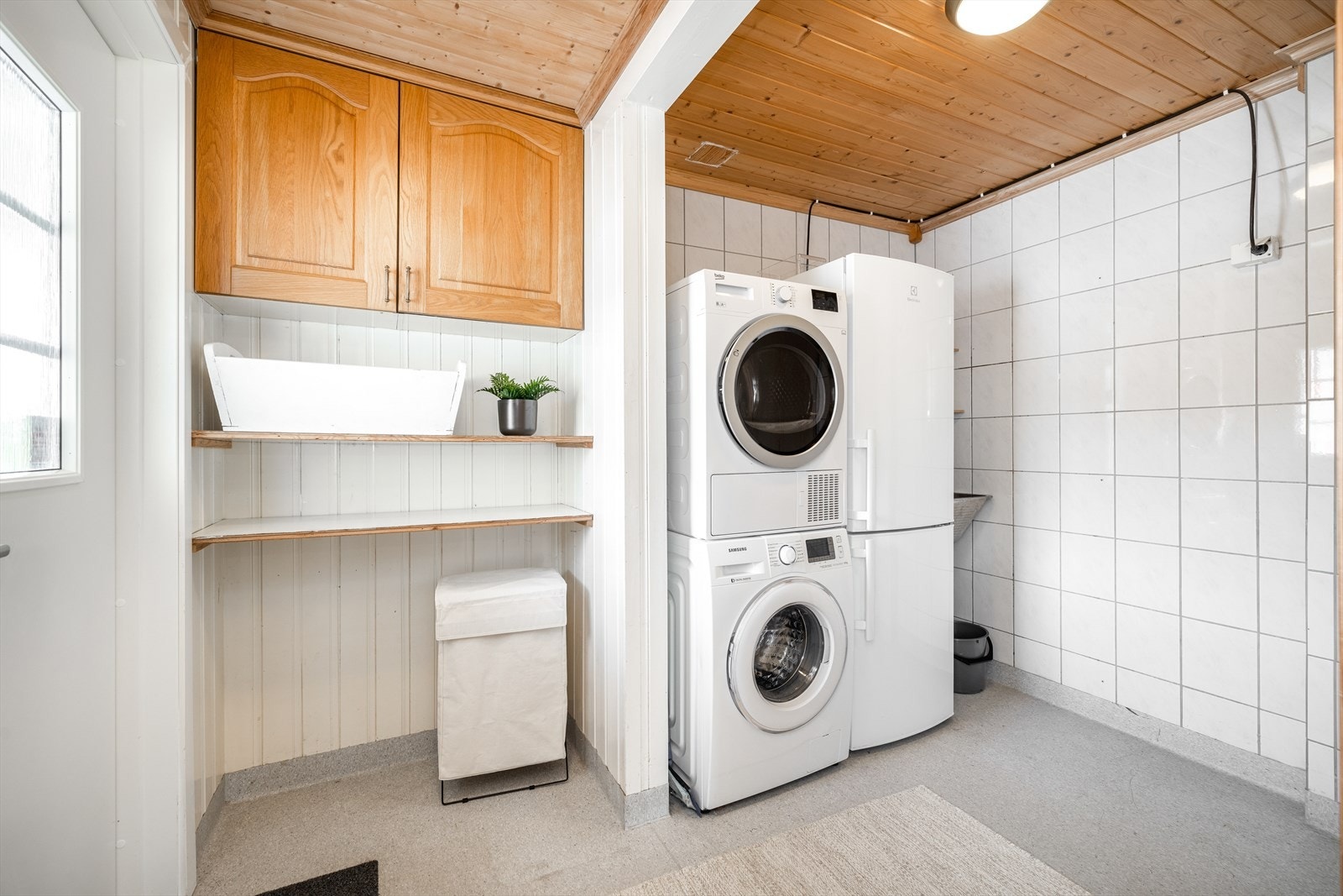 Praktisk innredet vaskerom med egen sone for vaskemaskin og tørketrommel. Fin plass til vaskeartikler i overskap og på fastmonterte hyller. Vaskerommet har belegg på gulv med varmekabler og fliser på veggoverflater. Det er utgang direkte ut til tunet. Galleribilde