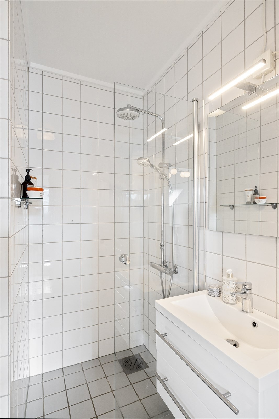 Badet er utstyrt med dusjhjørne med innfellbar dusjdør, gulvmontert toalett og baderomsinnredning med skuffer, servant og blandebatteri fra Grohe. Galleribilde