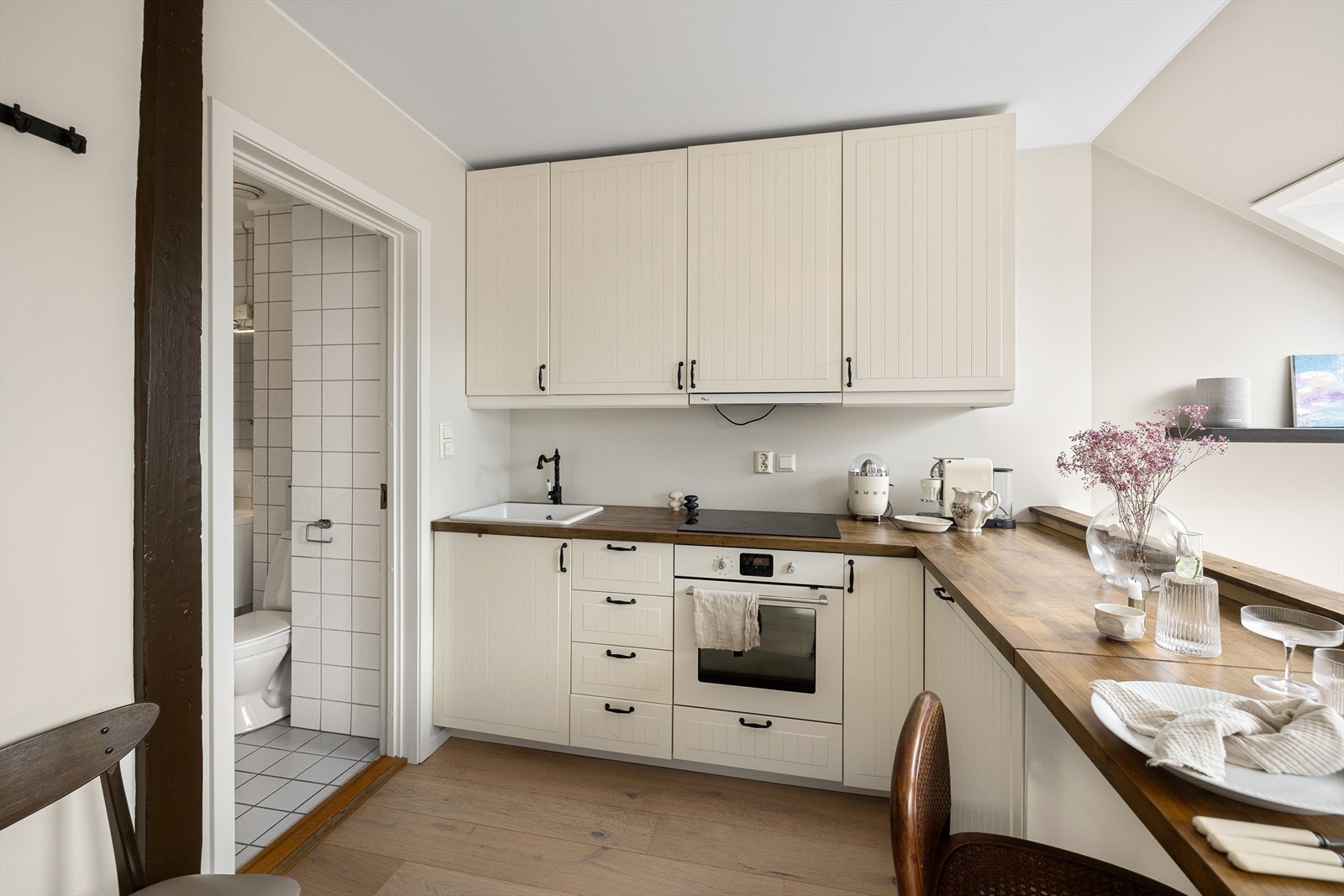 Lys innredning med profilerte fronter med skaper opp til himling og heltre benkeplate. Integrerte hvitevarer med platetopp, stekeovn og kjøleskap. Galleribilde