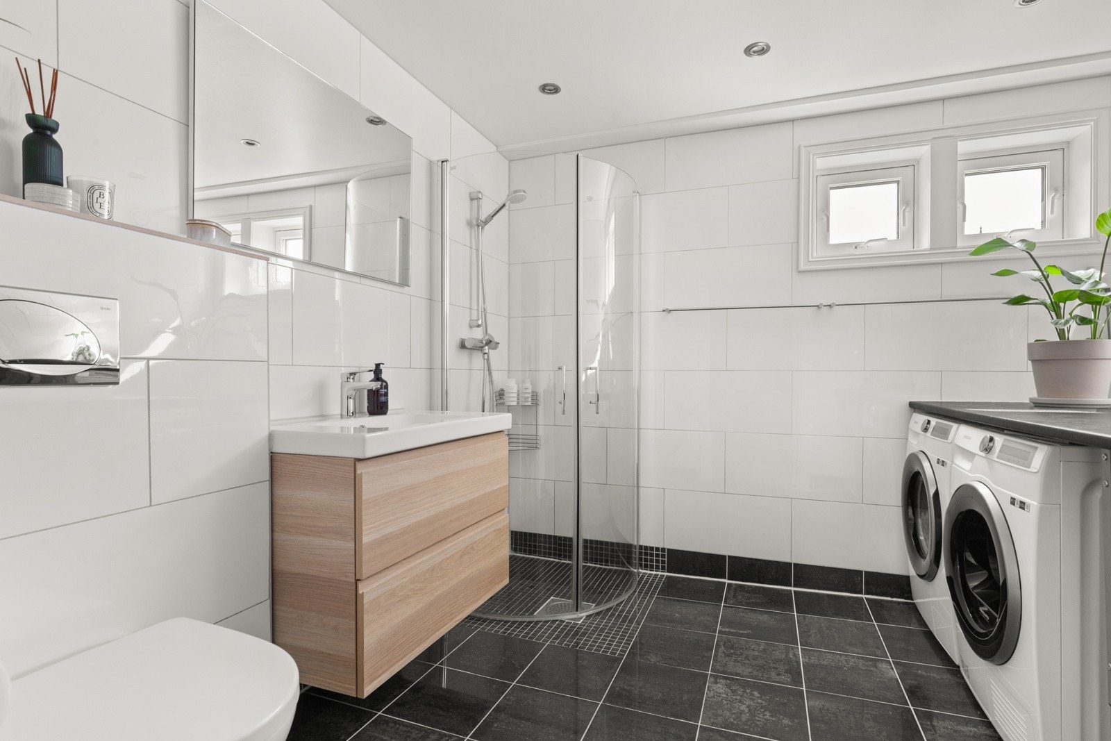 Badet er utstyrt med dusj med innfellbare glassvegger, servantseksjon med skuffer og heldekkende porselensvask, speil og vegghengt wc. Galleribilde