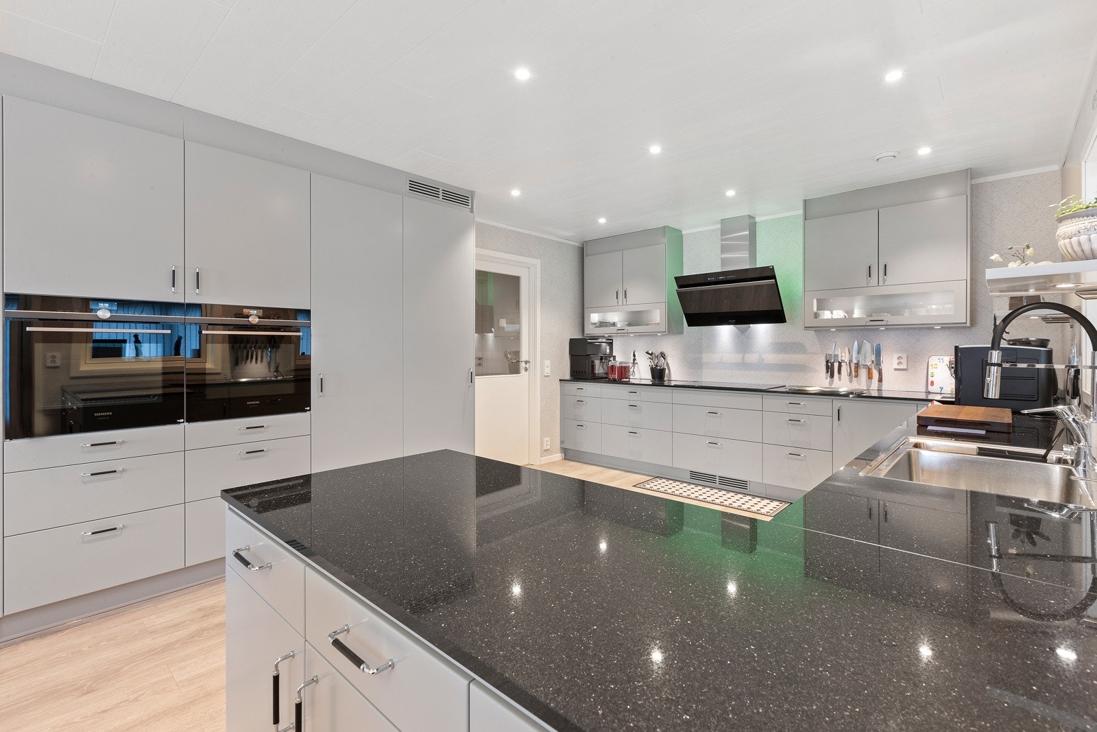 Lekkert og åpent kjøkken fra Drømmekjøkken med glatte fronter og benkeplate av stein. Galleribilde