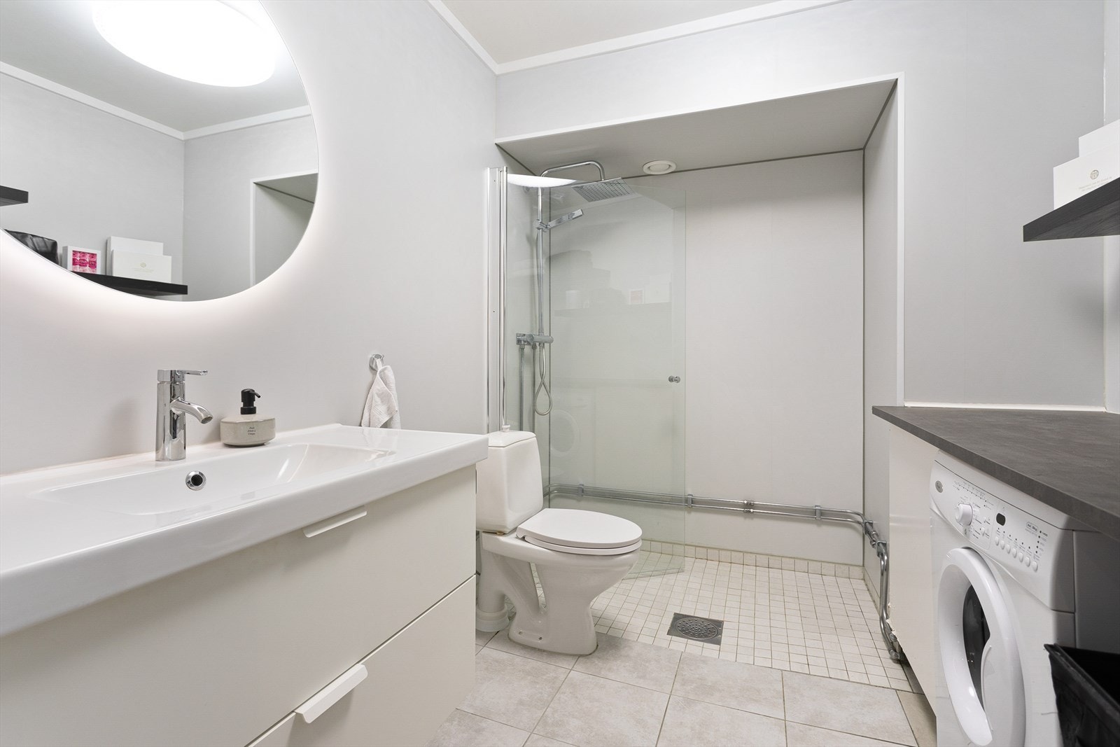 Flislagt bad innredet med servant på innredning, toalett og dusjhjørne med glassvegger. Galleribilde