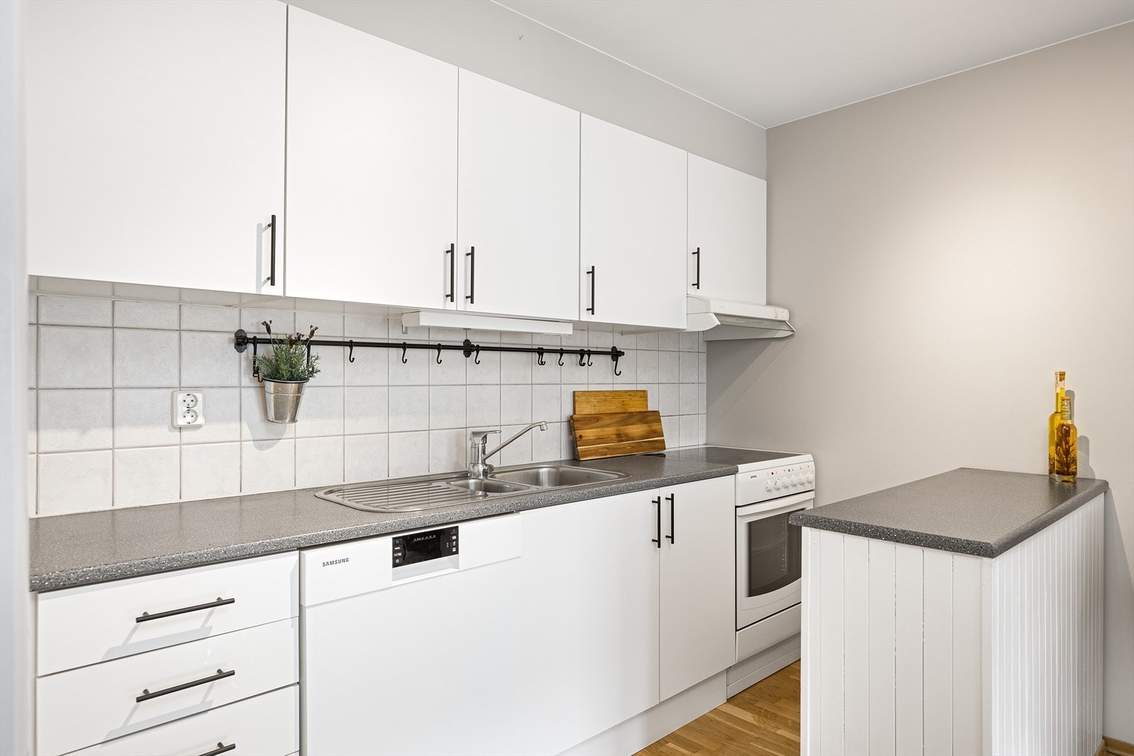 Hjemmet har et stort og innholdsrikt kjøkken med hvite, slette fronter og hvitevarer fra blant annet Samsung. Her har man godt med skap- og benkeplass, og en praktisk kjøkkenøy som bidrar til flere gunstige arbeidssoner. Galleribilde