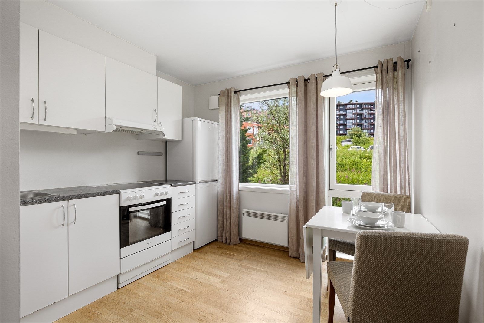 Kjøkkenet ligger adskilt til, og har hvite, slette fronter og godt med skap- og benkeplass. Her kan man enkelt innrede med et spisebord med klaff eller ileggsplater slik at det kan gjøres større ved behov. Alle hvitevarer på kjøkken vil følge handelen. Galleribilde