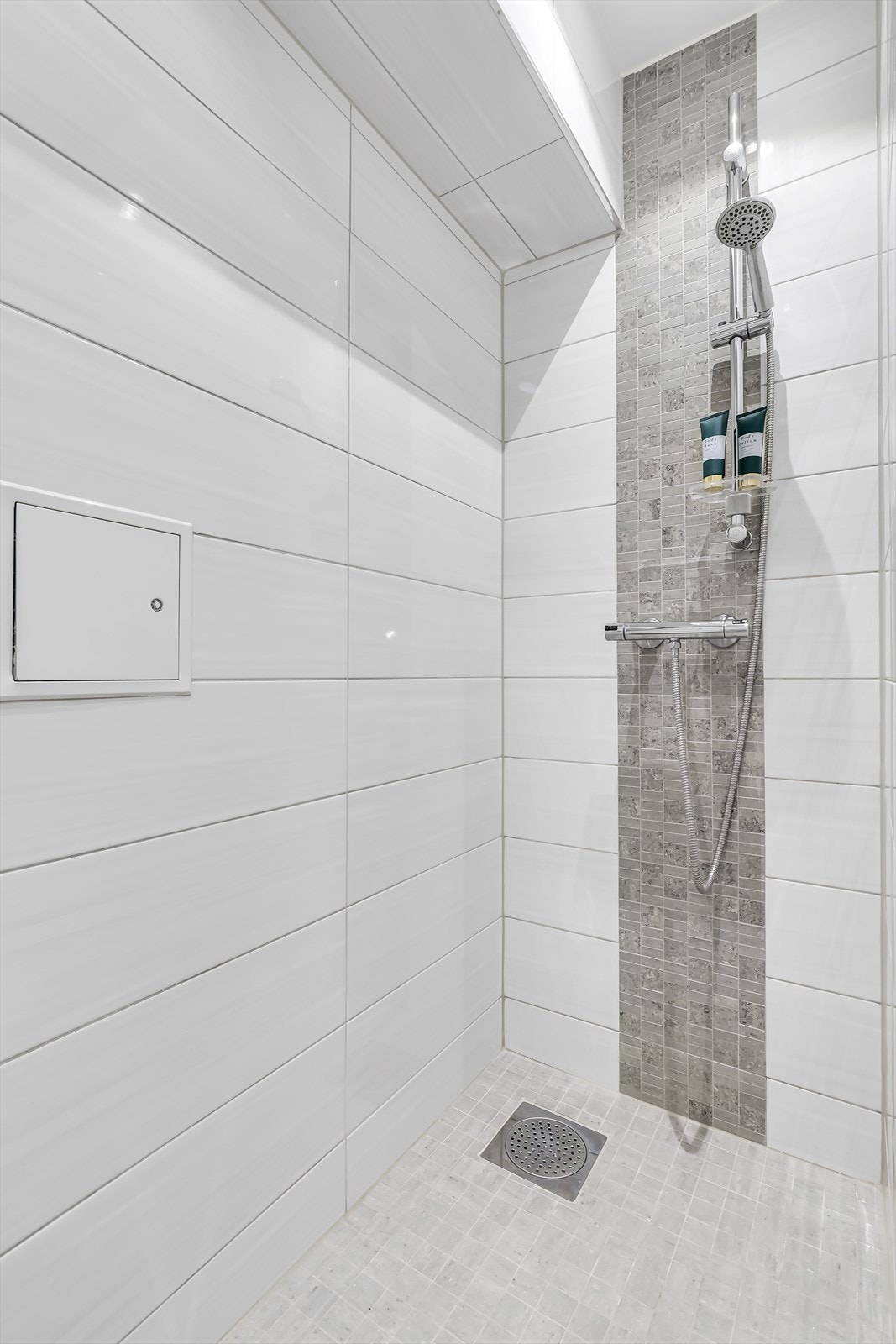 Moderne og romslig dusjområde med fliser på vegger og gulv, med flott dusjhode og armatur med holder til såpe. Galleribilde