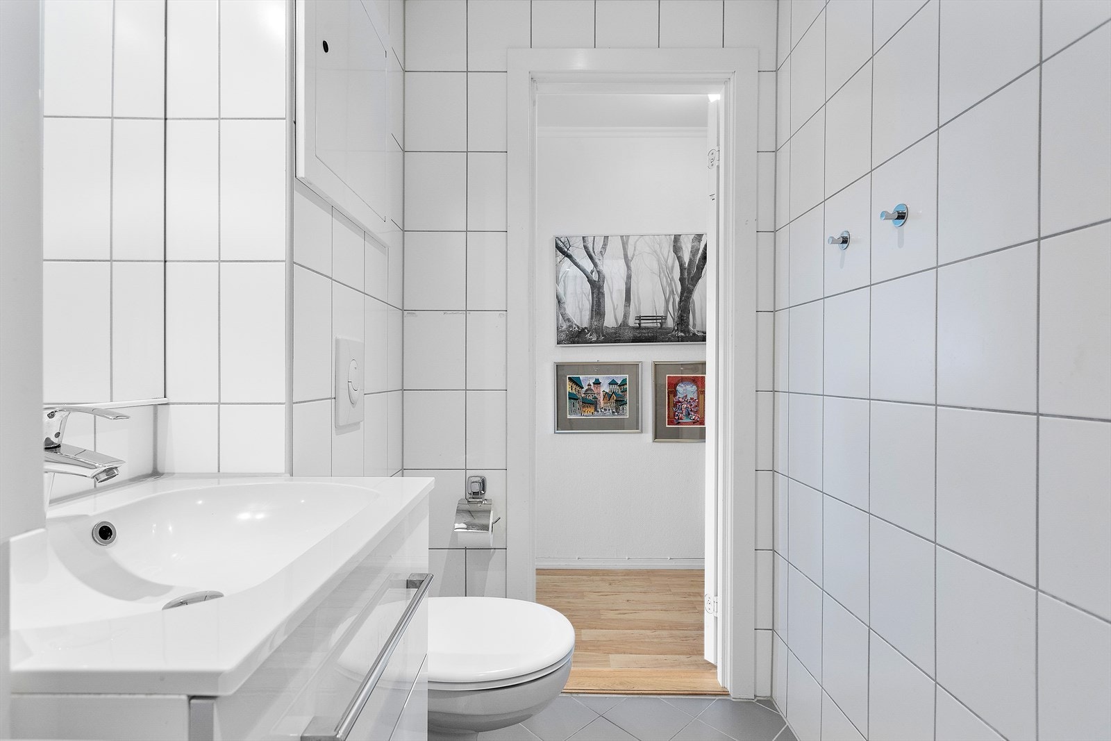 Badet er oppusset med vegghengt toalett, delikate lyse fliser og fin hvit baderomsinnredning. Galleribilde