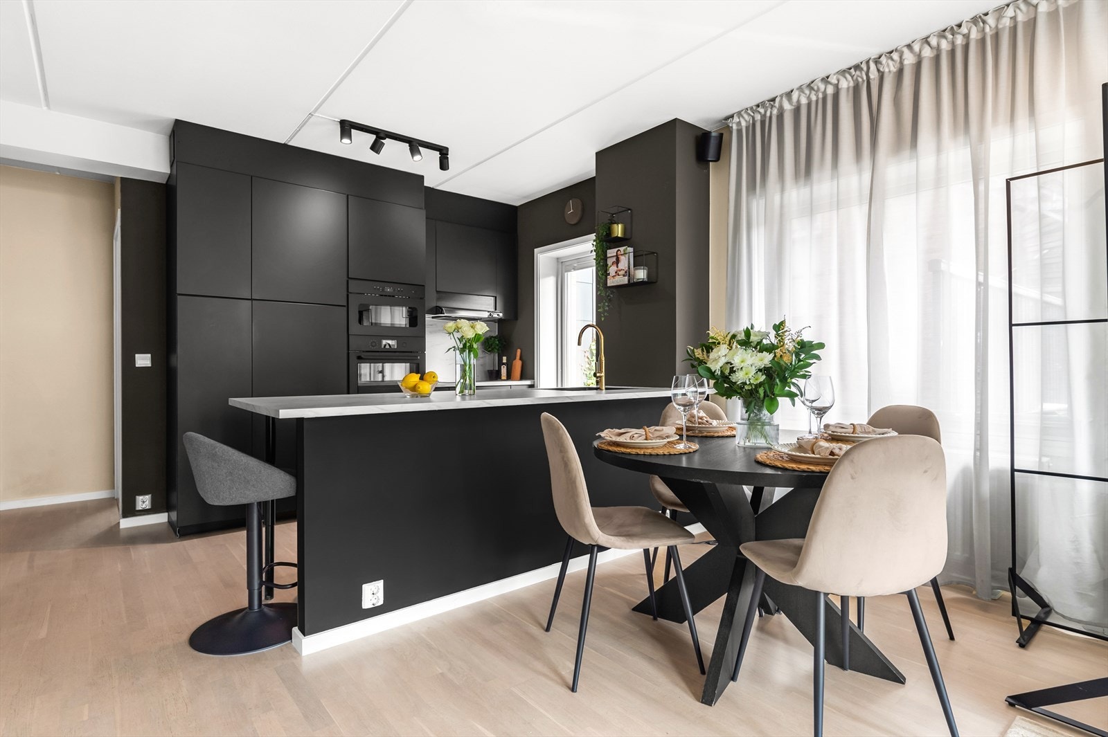 Lekkert kjøkken med slette overflater i dempet sort. Kjøkkenøyen skaper et skille mellom stue og kjøkken Galleribilde