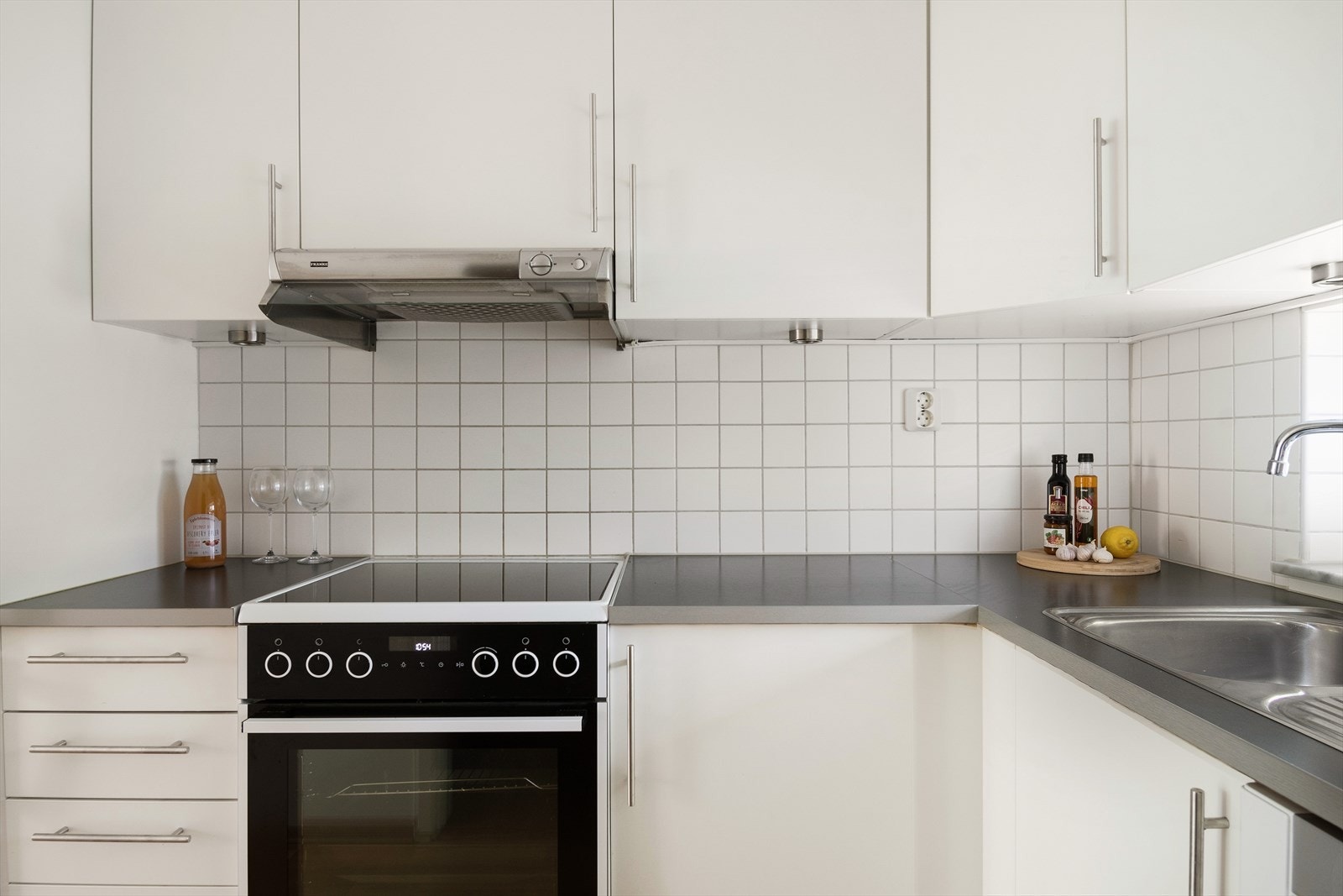 Pent kjøkken fra byggeåret med hvite fronter, fliser på bakvegg og laminert benkeplate. Galleribilde