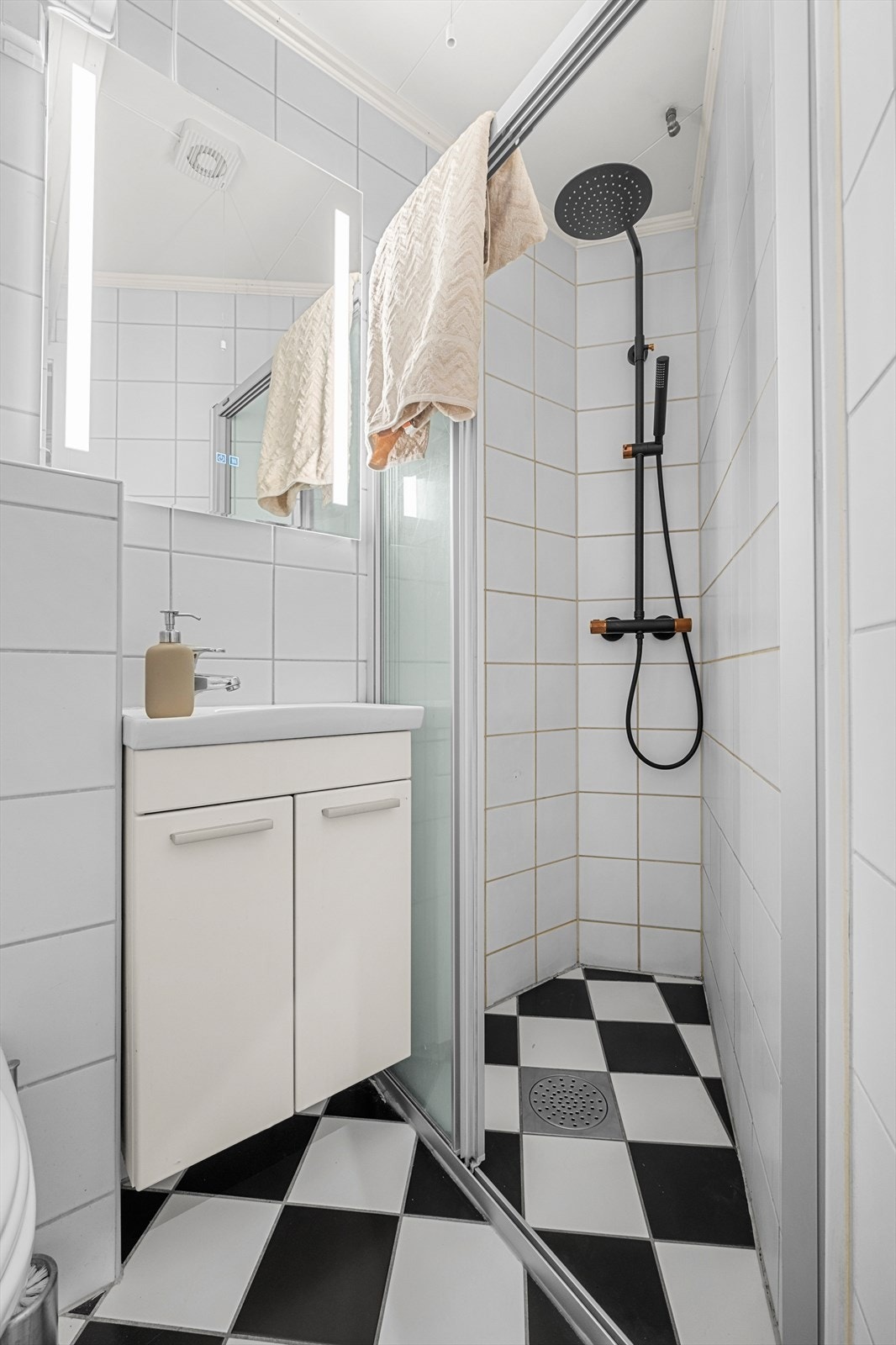 Her får du moderne baderomsinnredning med regndusjarmatur i tidsriktige farger, sjakkrutete fliser på gulv med varmekabler samt et helt nytt speil med ledbelysning. Galleribilde