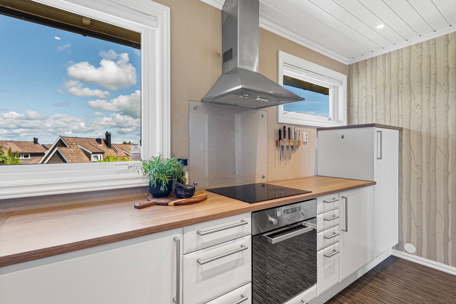 Slette fronter og benkeplate av laminat. Det er montert glassplate på vegg bak vask og platetopp. Galleribilde