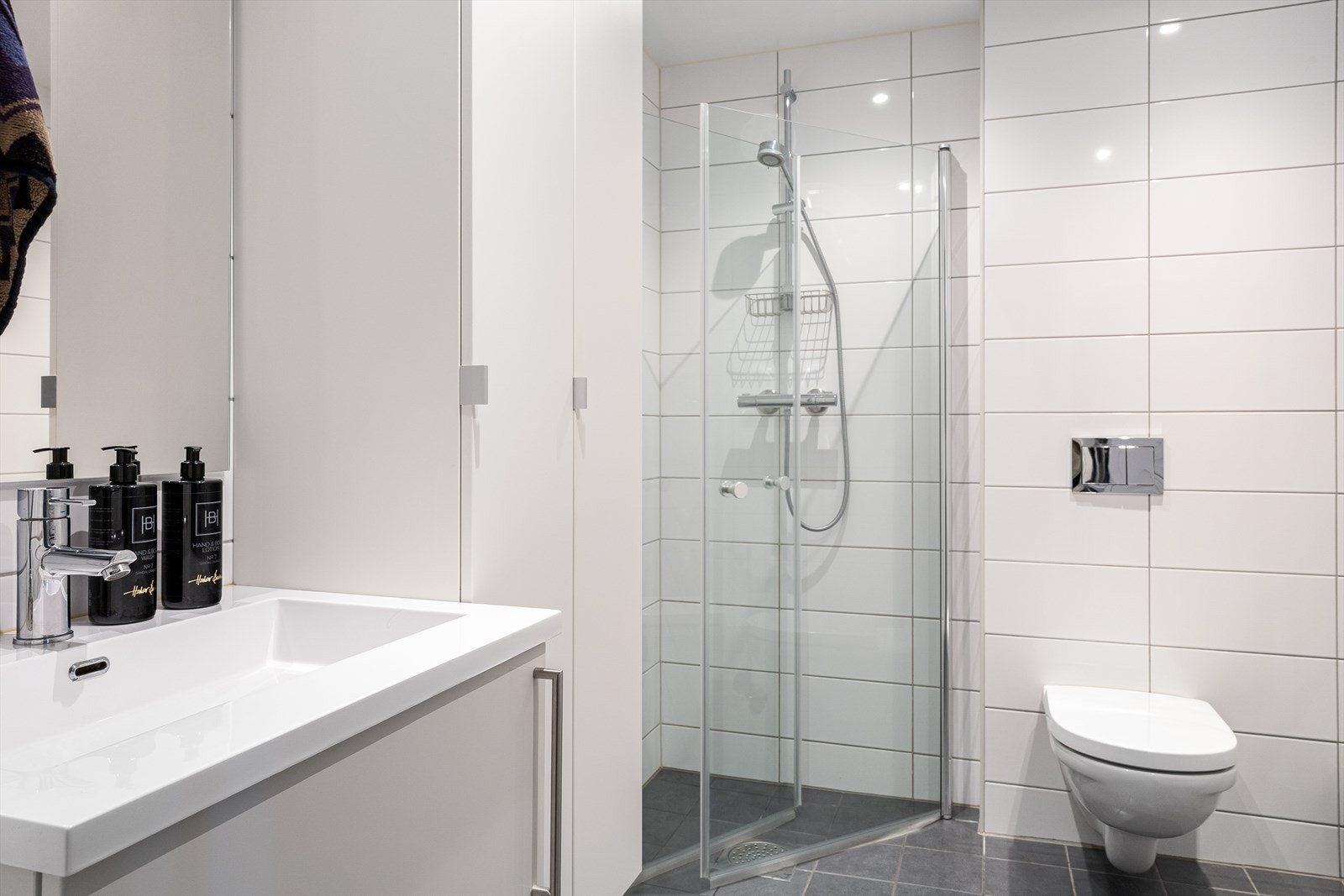 Badet er innredet med vegghengt klosett, servantinnredning med underskap, dusjhjørne med dører i glass og opplegg for vaskemaskin/tørketrommel. Galleribilde