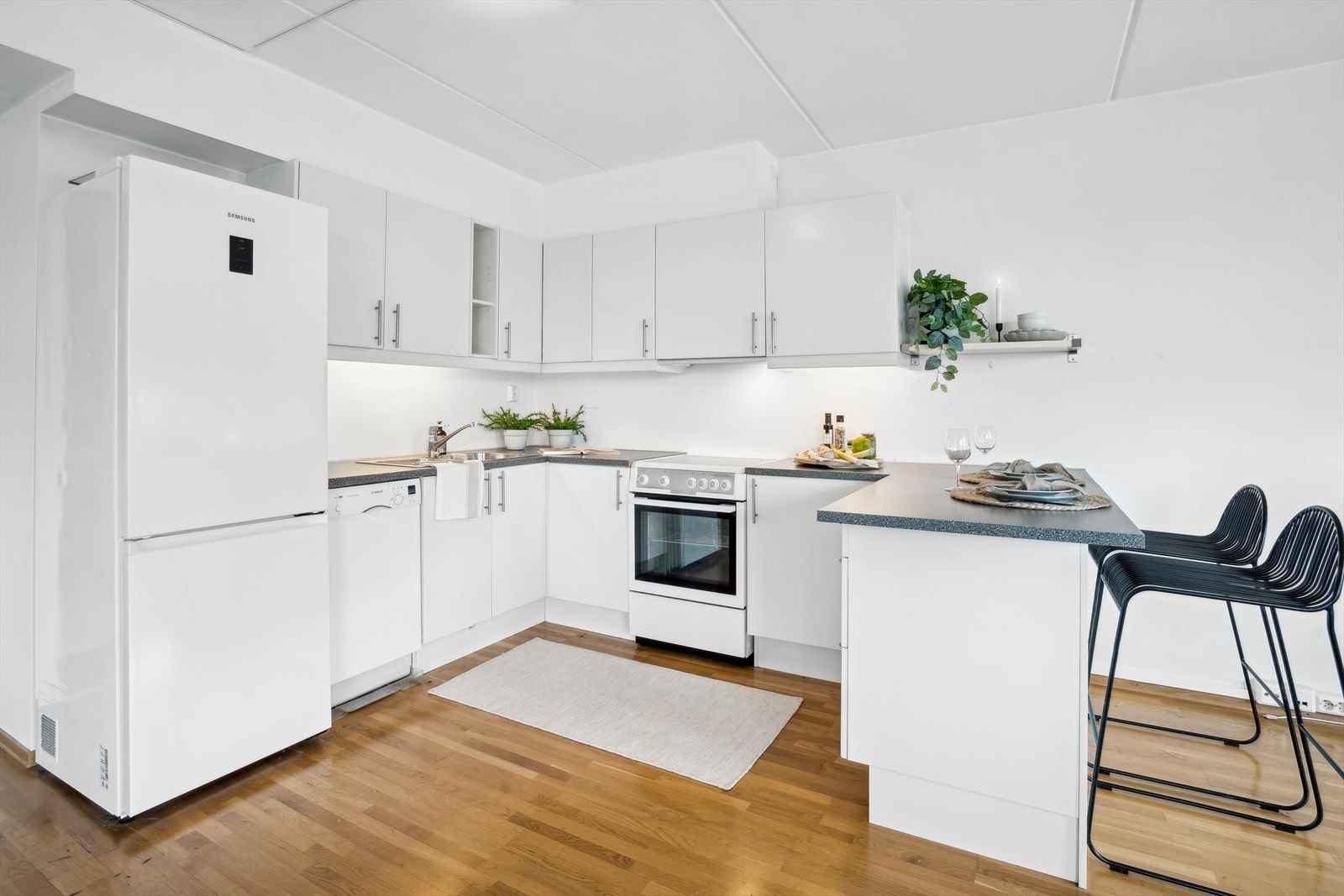 Kjøkkenet er i åpen planløsning mot stuen, med glatte, hvite fronter og en benkeplate av laminat. Innredningen er montert i en hesteskoform som gir god utnyttelse av rommet. Galleribilde