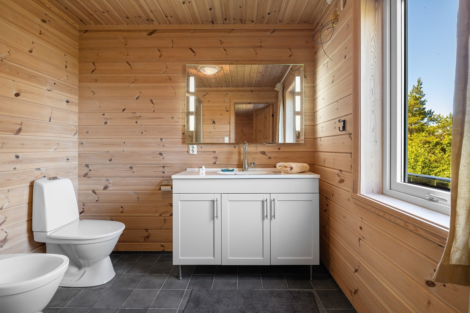 Det første badet har flislagt gulv med elektriske varmekabler og panel på vegger. Badet er ellers innredet med dusjkabinett, bidé, toalett og helstøpt servant med underskap. Galleribilde