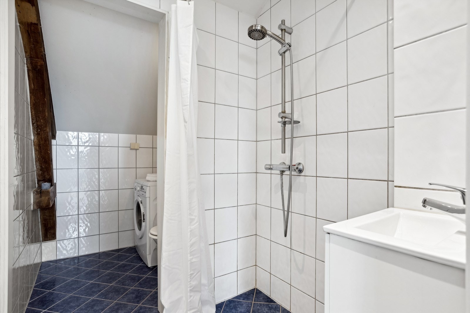 Badet i loftsetasjen består av frittstående toalett, servant med underskap, speil og åpen dusj med forheng, samt opplegg for vaskemaskin. Galleribilde