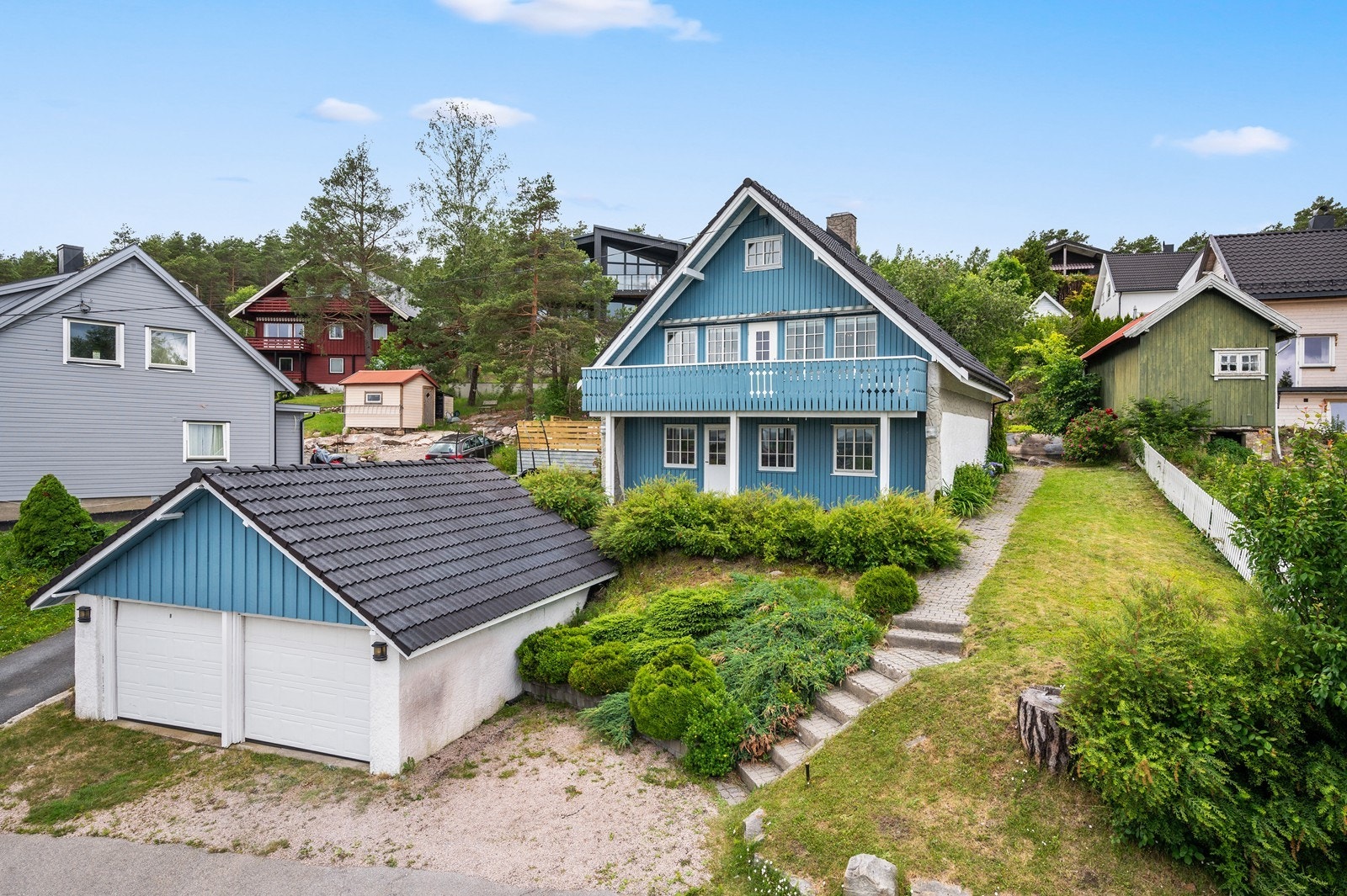 Enebolig med fritt liggende dobbelgarasje. Eiendommen har grøntarealer med gress og diverse beplantning. Galleribilde