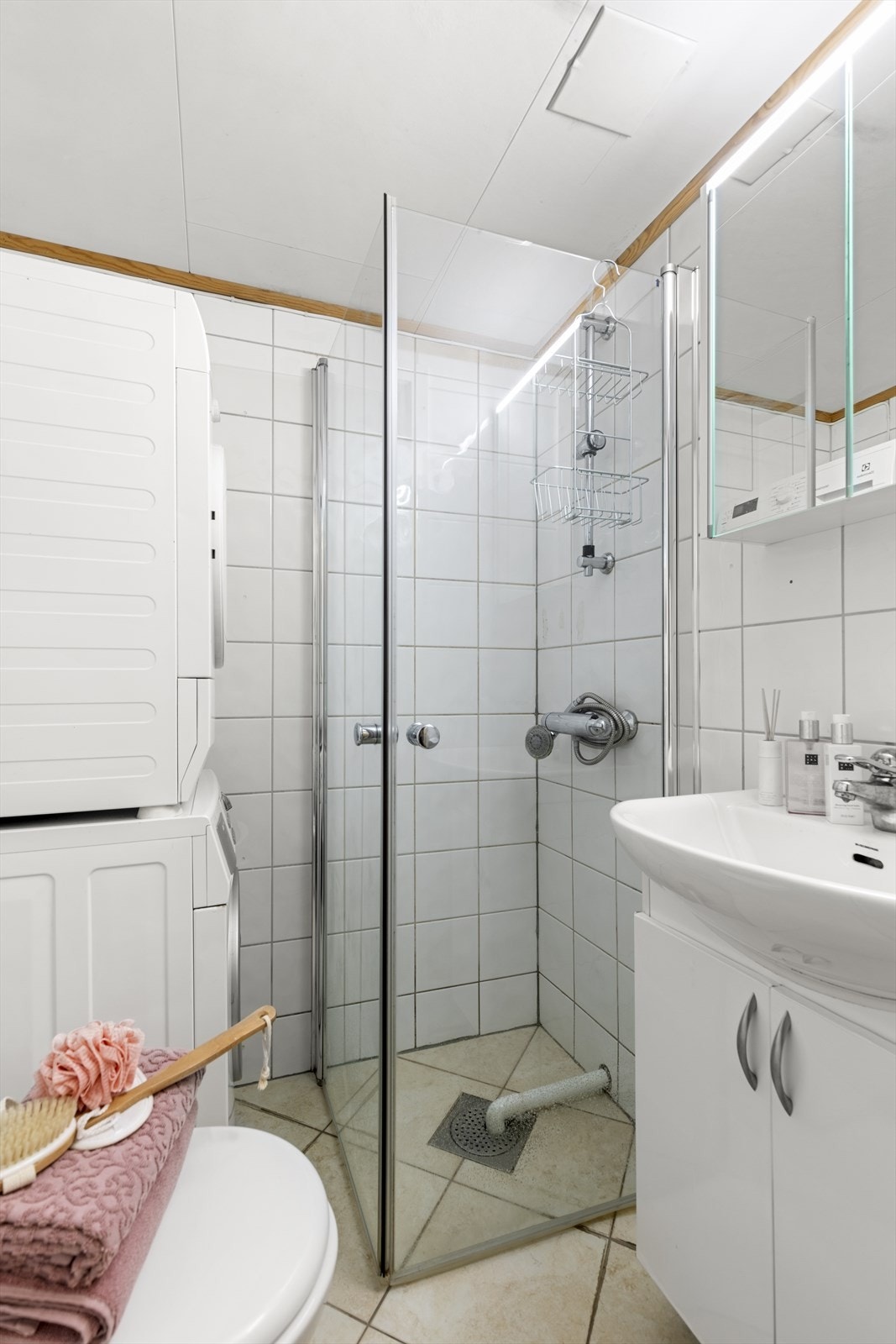 Flislagt bad med elektriske varmekabler i gulv. Rommet har innredning med nedfelt servant, veggmontert toalett, dusjvegger/hjørne og opplegg for vaskemaskin. Galleribilde