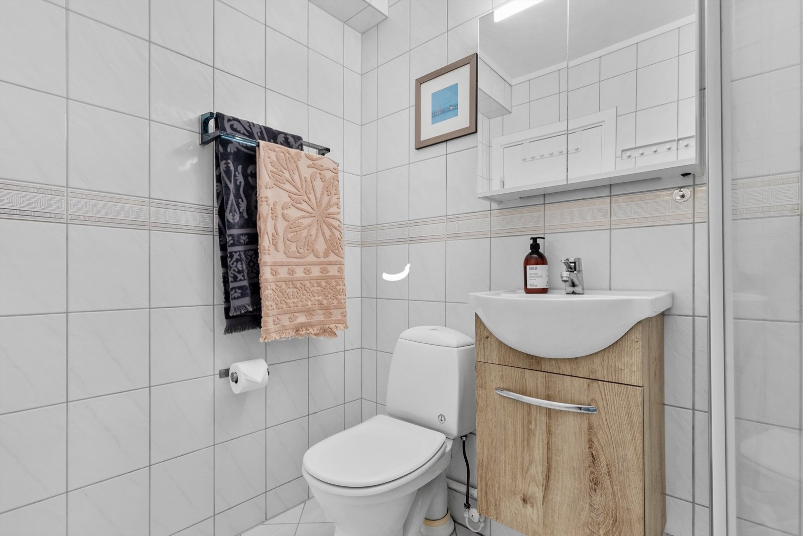 Badet er innredet med gulvstående toalett, servant på benkeskap, speilskap og dusjkabinett. Det er opplegg for vaskemaskin på badet. Galleribilde