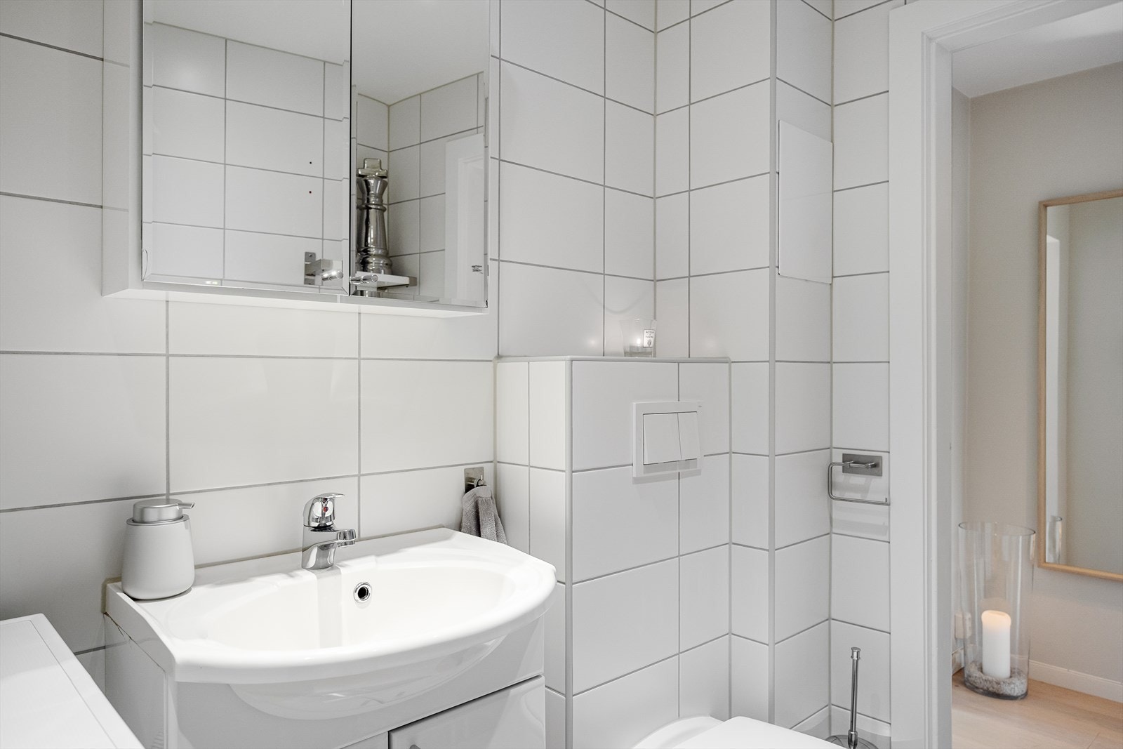 Badet består av servantskap med nedfelt servant, veggskap med speildører og lys over, vegghengt klosett med innebygd sisterne og dusjsone med innfelte dusjdører i herdet glass. Det er opplegg for vaskemaskin. Galleribilde