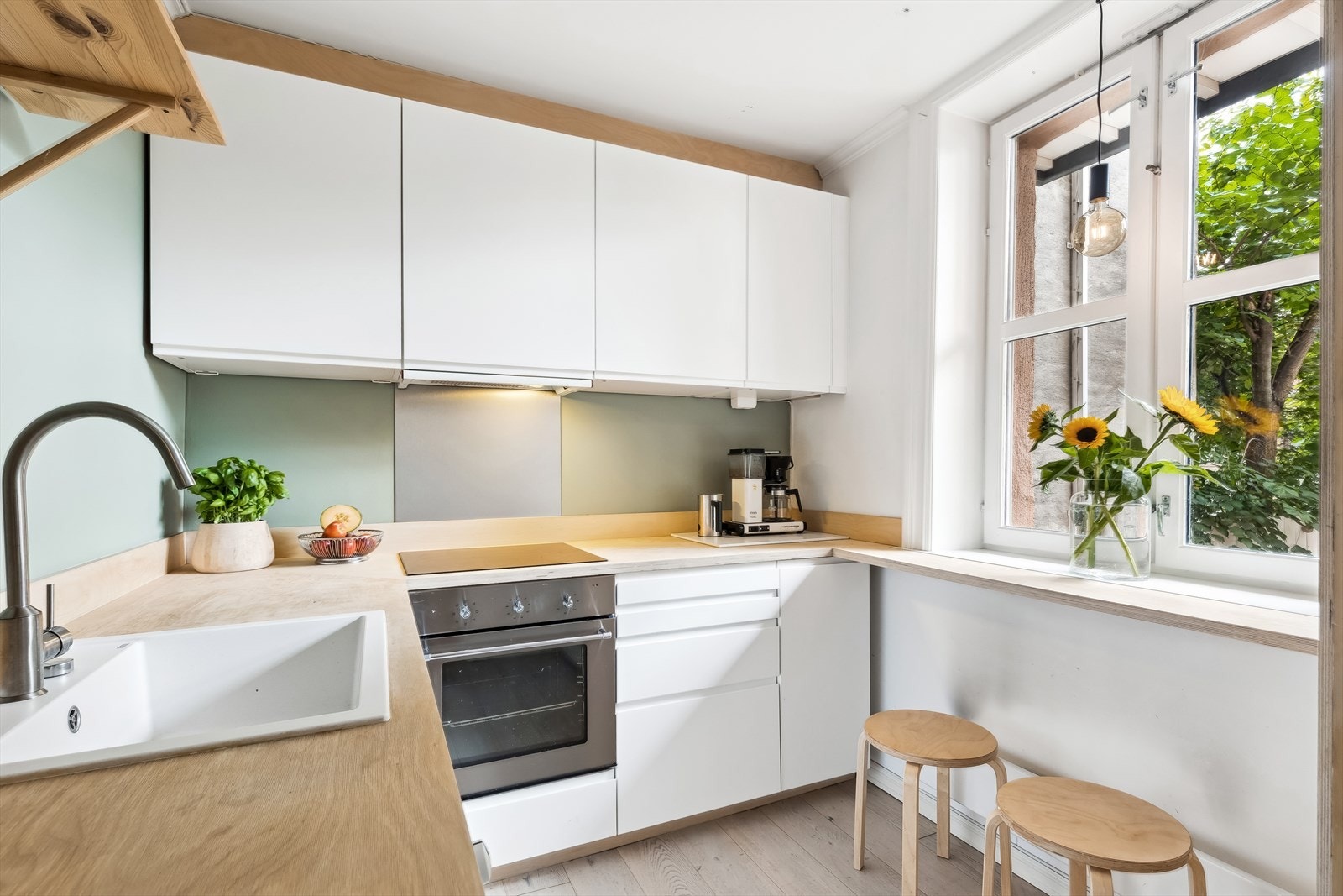 Kjøkkeninnredning med glatte fronter og stålplate på vegg over benkeskap. Heltre benkeplate med kum. Ventilator. Induksjonstopp og stekeovn er integrert i innredningen. Galleribilde