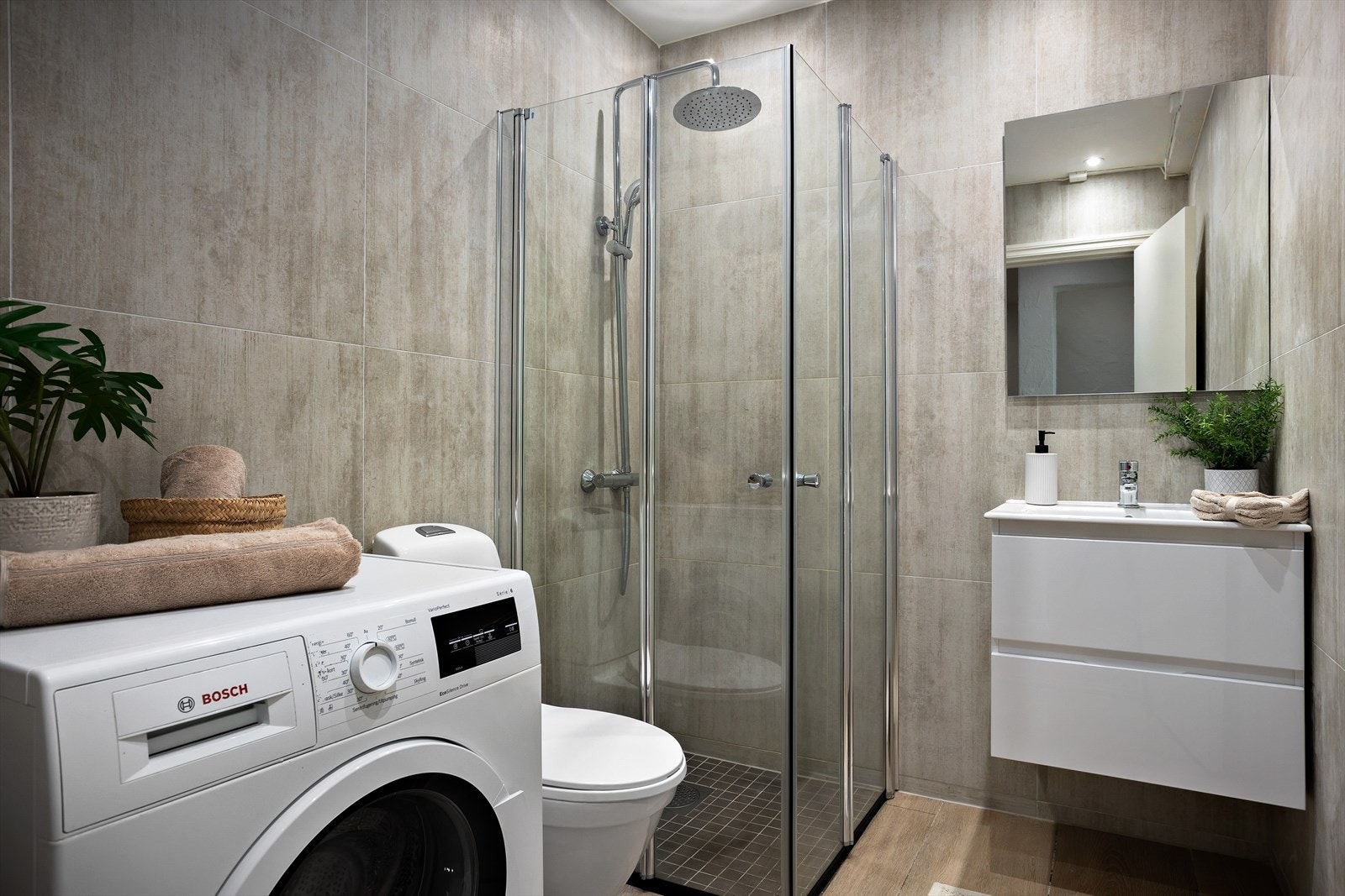 Delikat bad bestående av flislagte gulv med varmekabler, flislagte vegger, gulvstående toalett og vegghengt servantinnredning Galleribilde