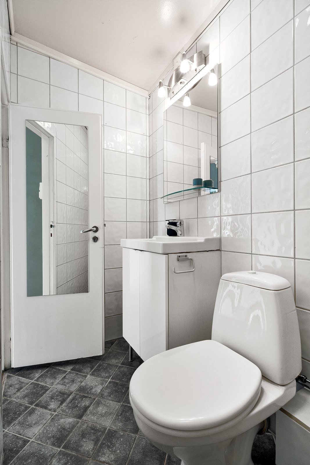 Flott flislagt baderom fra 2004. Badet består av servantskap med glatte fronter, heldekkende servant, speil og lysarmatur på veggen over servanten. Galleribilde