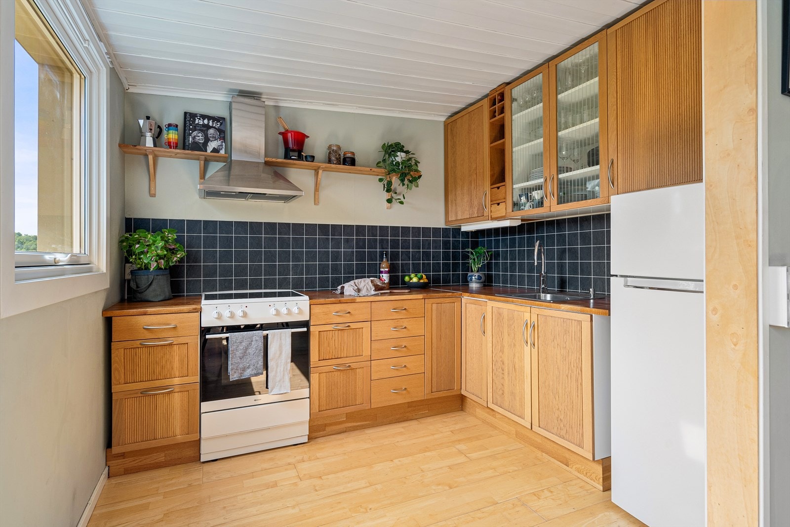 Flott kjøkken med god skap- og benkeplass. Kjøkkenet har profilerte fronter, heltre benkeplate med nedfelt kum, flislignende plater på vegg over benk og lys under overskap. Galleribilde