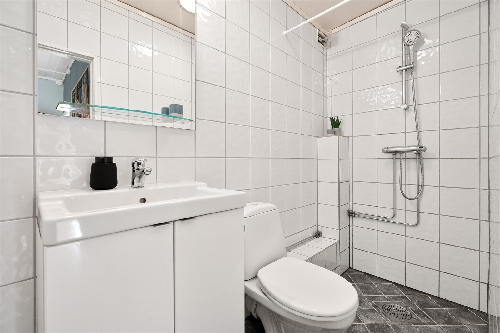 Videre er det gulvmontert klosett med utenpåliggende sisterne og dusjhjørne med forheng. Galleribilde