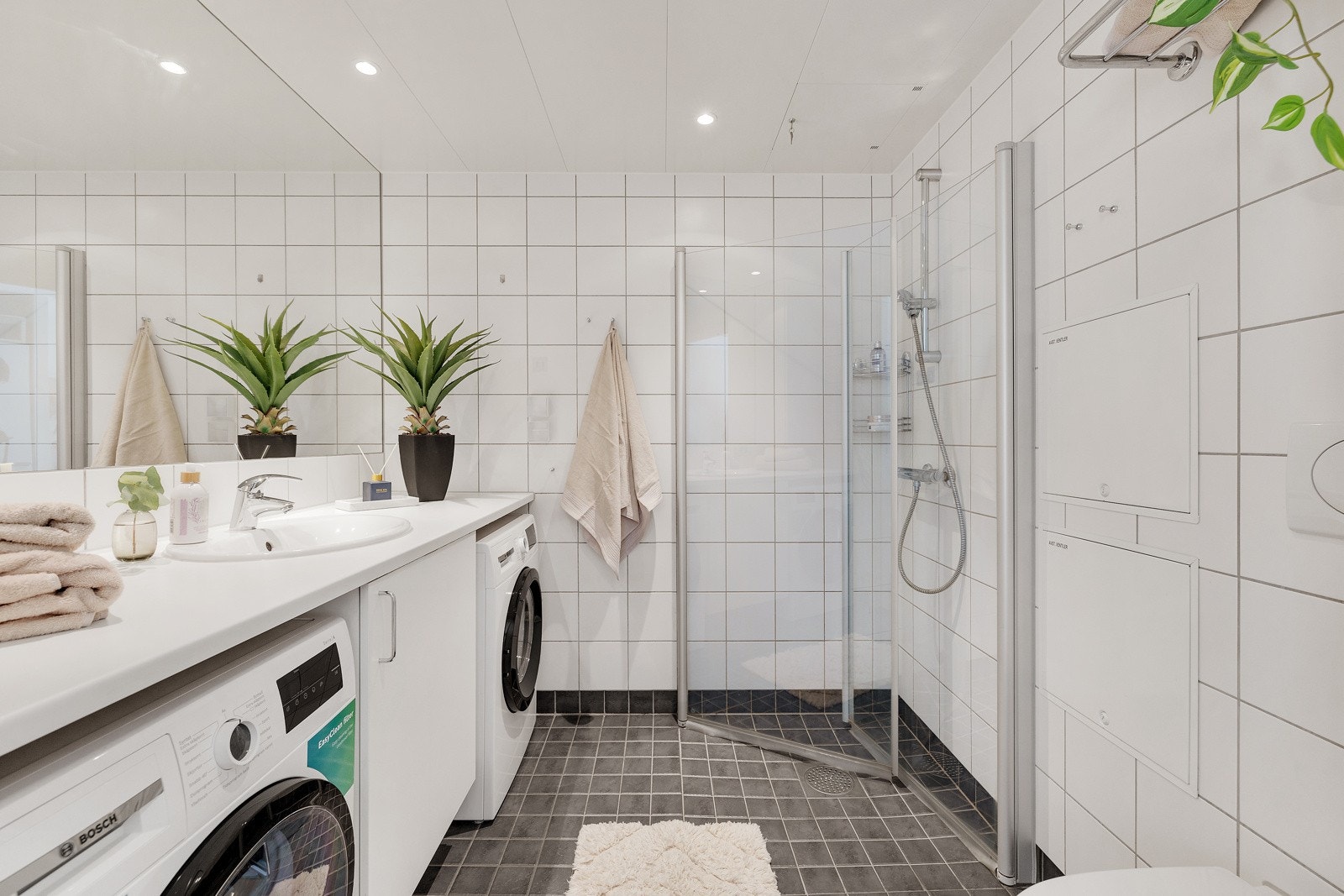 Moderne og flislagt bad med elektriske varmekabler i gulv, opplegg for vaskemaskin og tørketrommel og innfellbare dusjdører. Galleribilde