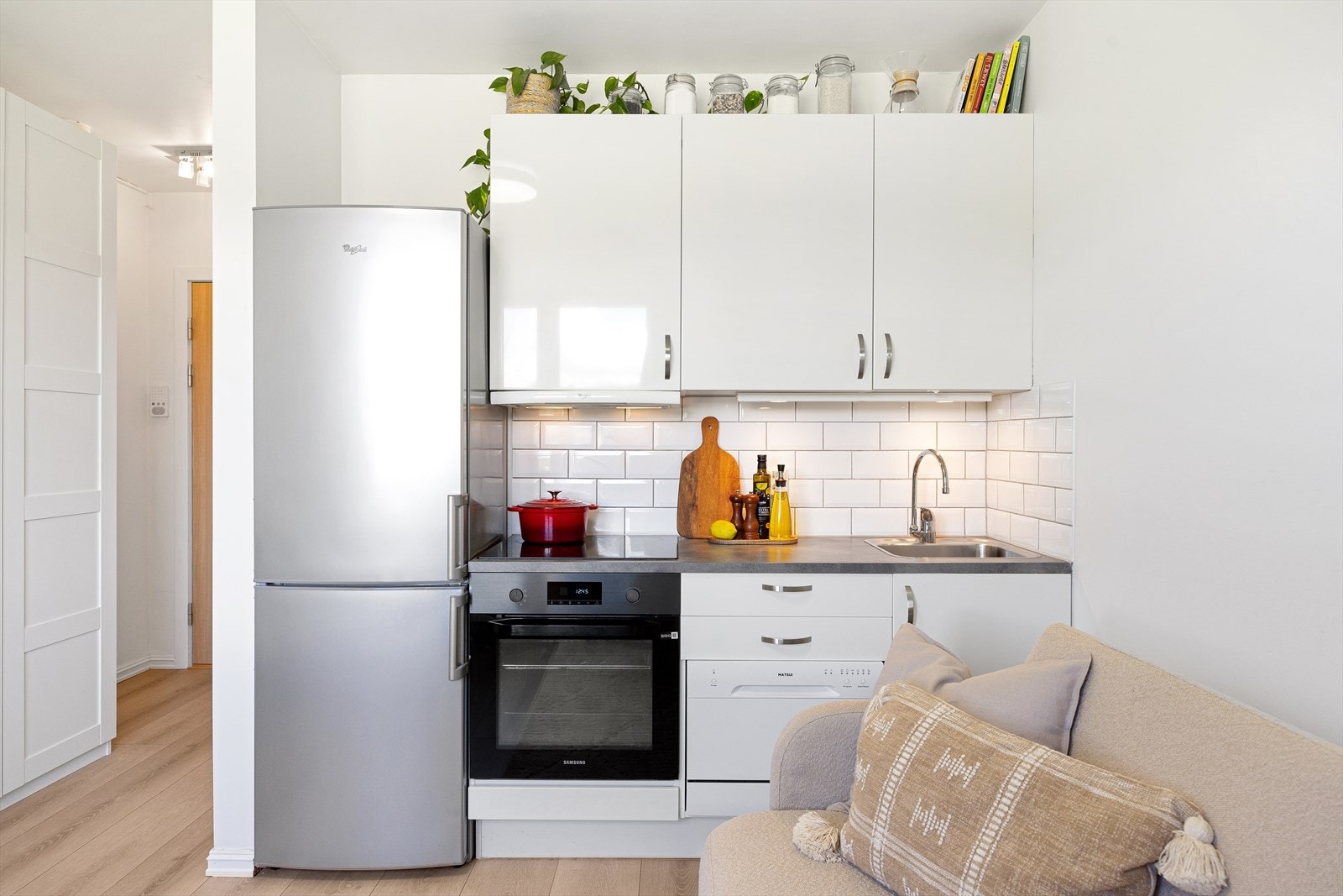 Moderne og stilren kjøkkeninnredning bestående glatte laminerte fronter, fliser mellom overskap og laminert benkeplate, lys under overskap, kullfiltervifte over integrert koketopp, kum med ettgreps blandebatteri og opplegg vaskemaskin. Galleribilde