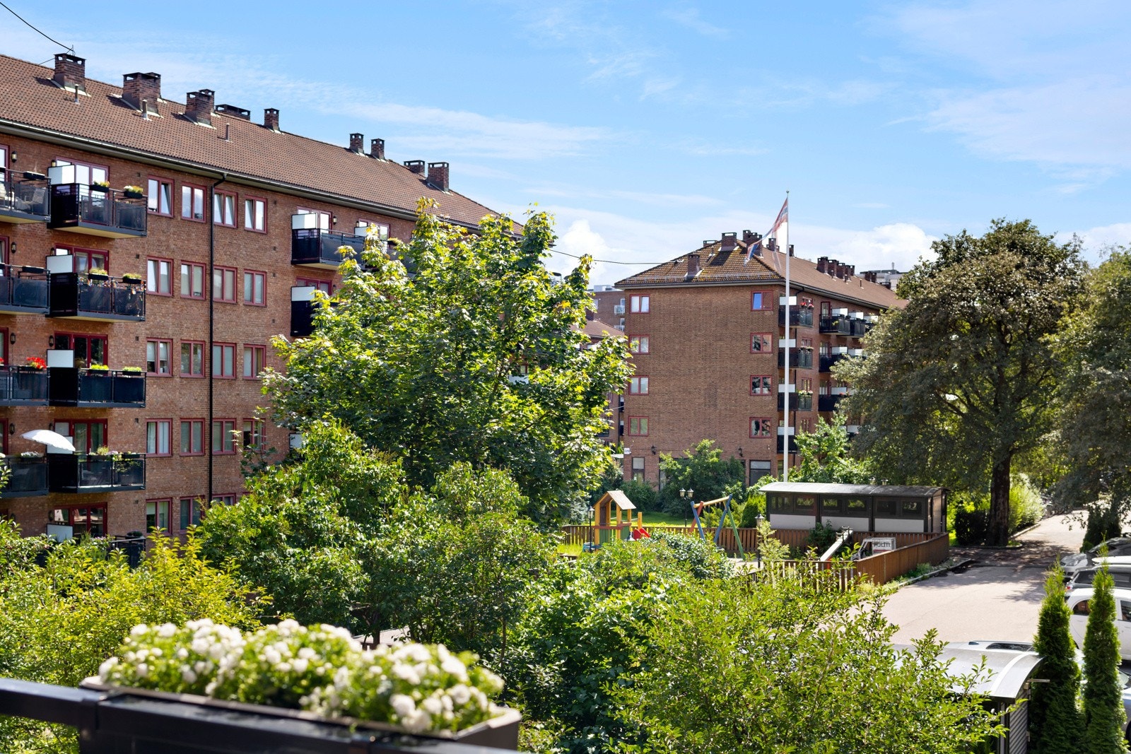 Hyggelig utsyn fra balkongen over borettslagets fellesarealer som er pent opparbeidet med flotte blomster, busker og gressplen Galleribilde