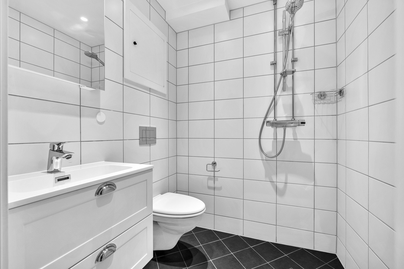 Pent bad med større hvite fliser på vegg og mørke fliser på gulv. Badet ble oppusset i 2018 i regi av borettslaget. Galleribilde