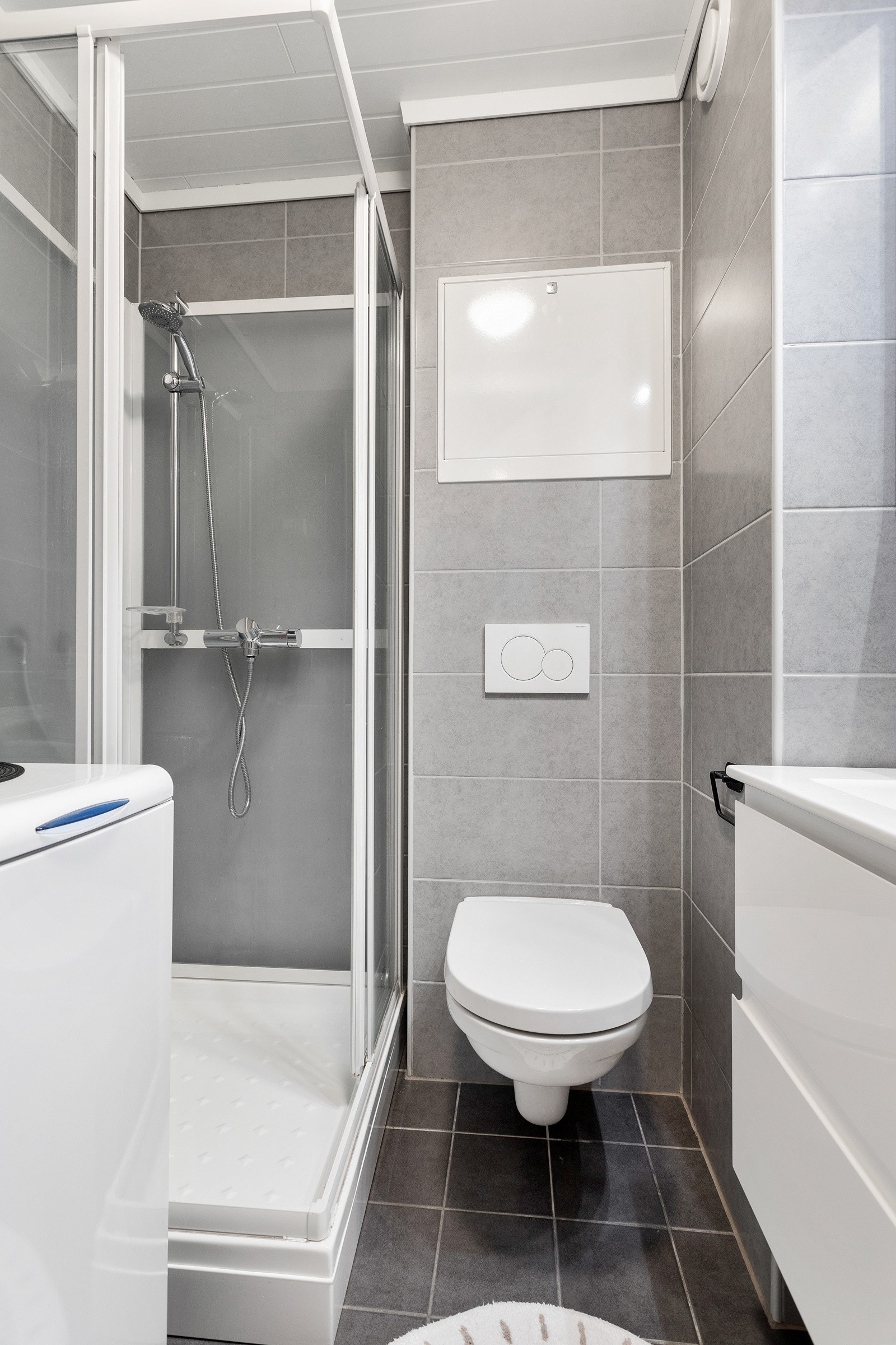 Badet er innredet med dusjkabinett, toalett, baderomsinnredning med servant og opplegg for vaskemaskin. Flislagt gulv med varmekabler. Galleribilde
