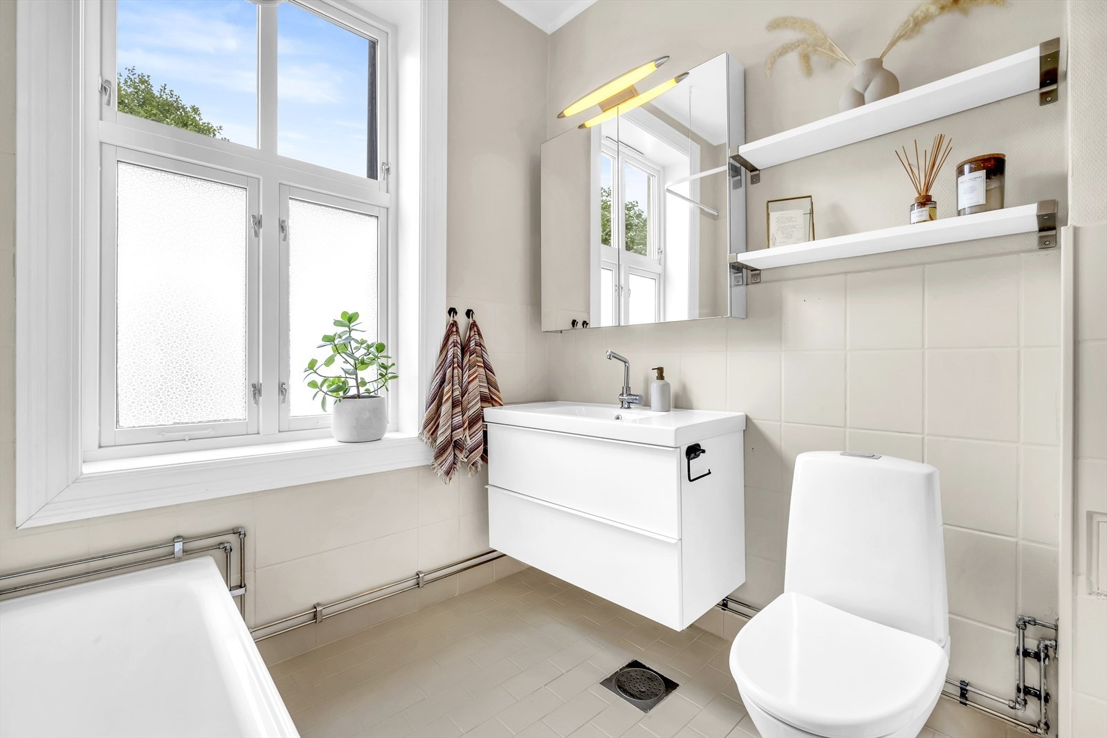 Badet er innredet med toalett, badekar og servant nedfelt i innredning og vegghengt speilskap Galleribilde