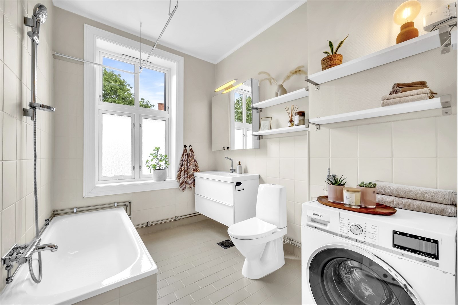 Tidløst bad med en kombinasjon av flislagte overflater og delvis malte vegger. Det er opplegg for vaskemaskin Galleribilde