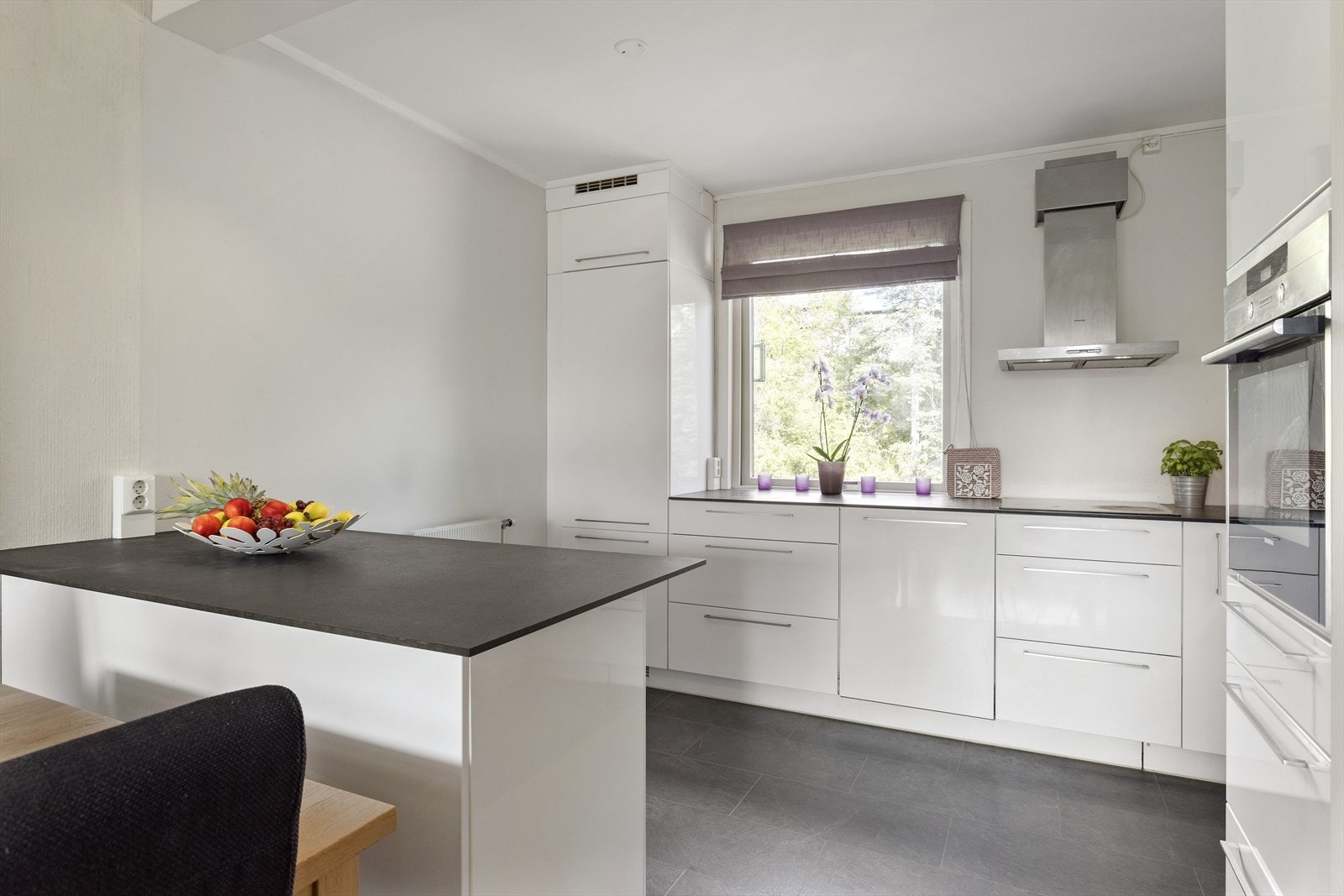 Kvik-kjøkken med hvite glatte fronter, kjøkkenøy, benkeplater i laminat og fliser over benkeskap Galleribilde