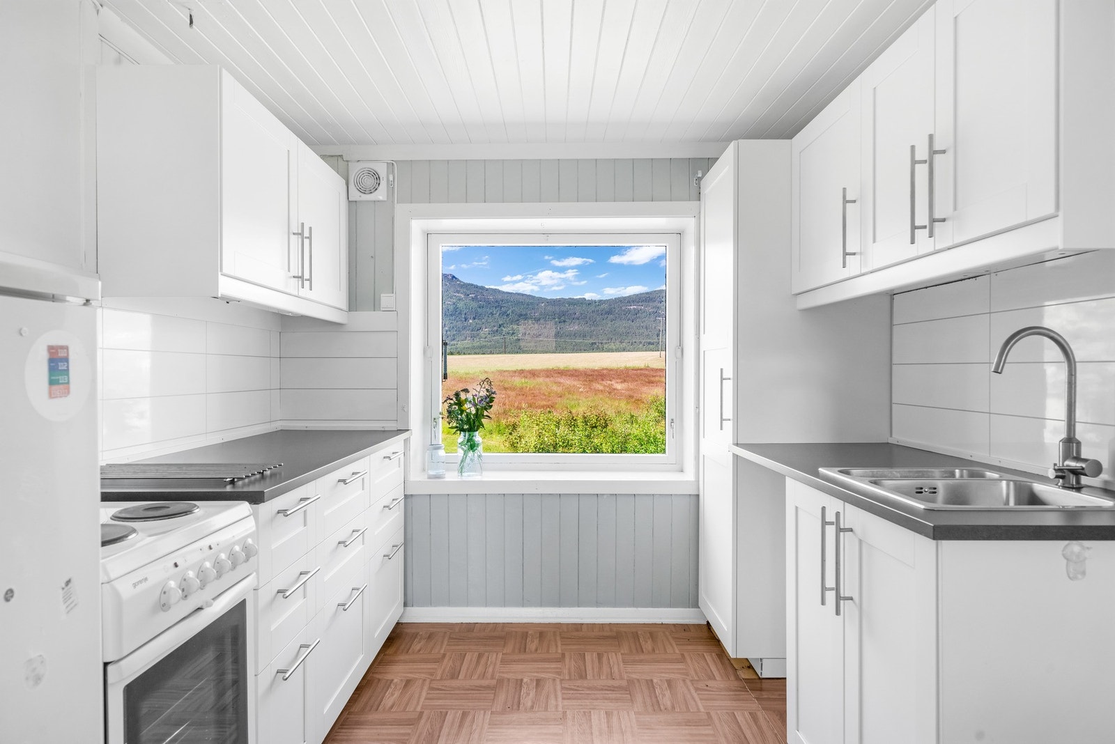 Kjøkken med innredning fra ca. 2017, gulv med belegg og vegger og tak med malt trepanel. Galleribilde