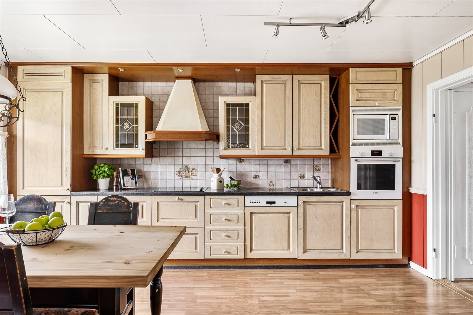 Innredningen har skuffer og takhøye skap med lyse, profilerte fronter og mørk benkeplate av laminat med flisfelt over. Galleribilde