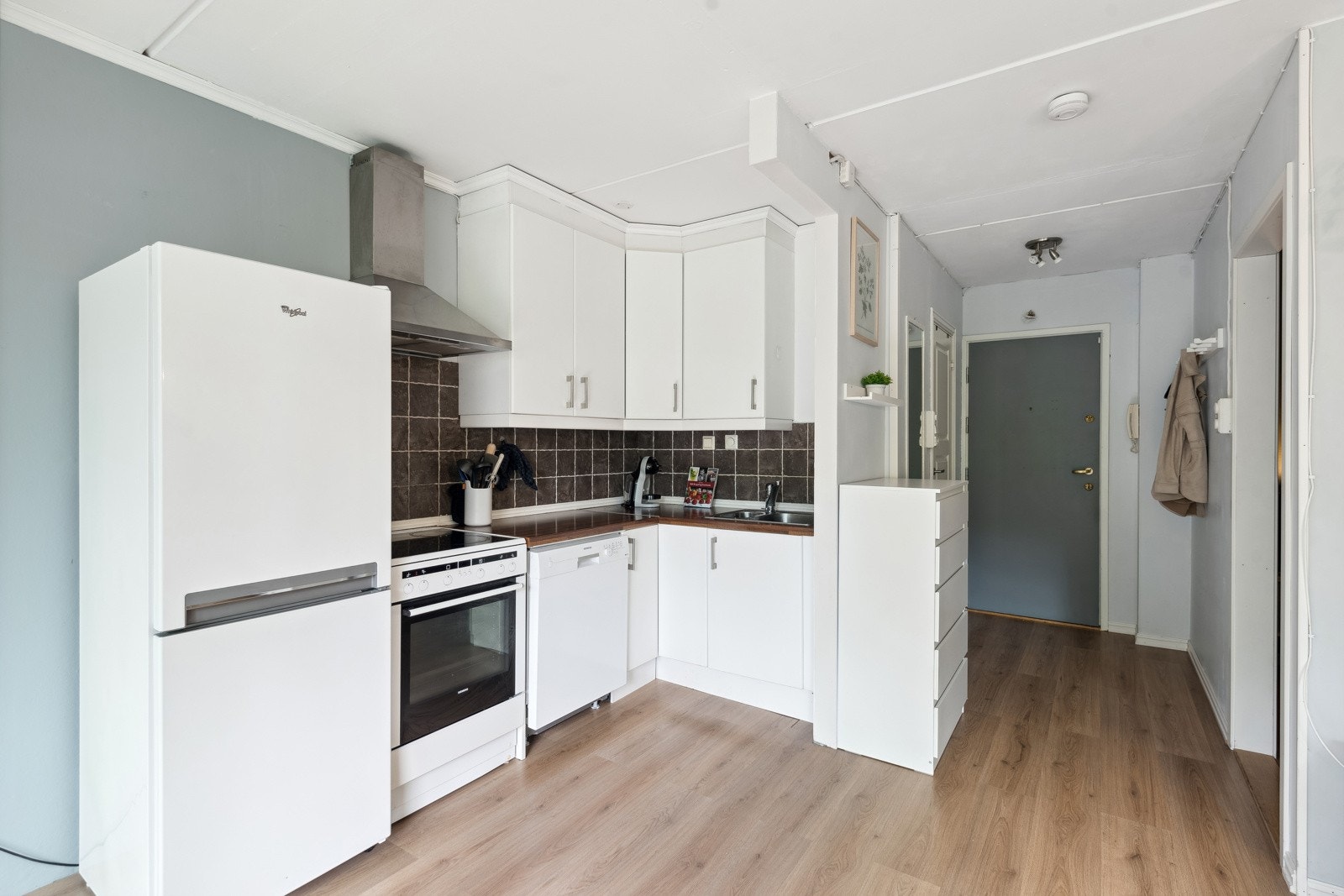 Kjøkkeninnredning med glatte fronter, benkeplater av laminat, nedsenket oppvaskkum med ett-greps armatur, flislagt mellom benkeplate og overskap. Galleribilde