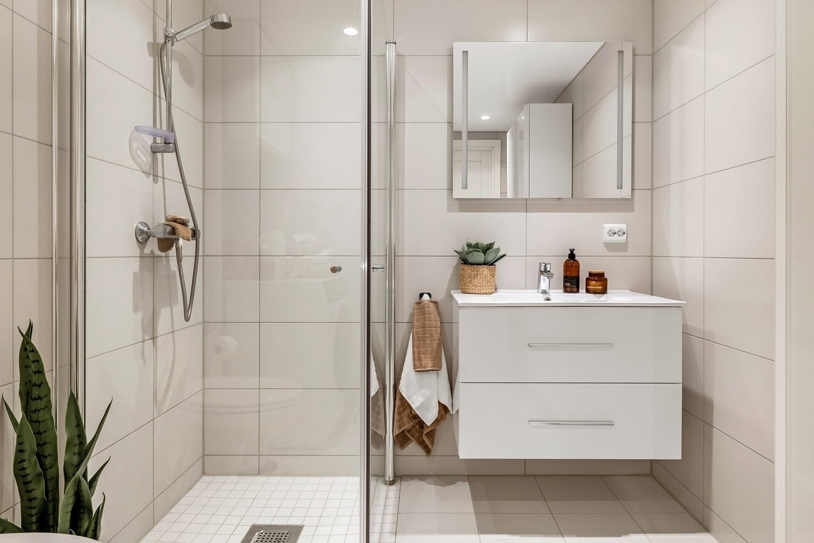 Badet innehar moderne baderomsinnredning, med romslig dusjhjørne, vegghengt toalett, servant i møblement, speil med belysning og oppbevaringsmuligheter. Galleribilde