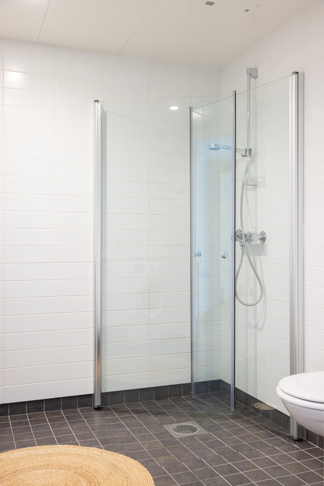 Badet er innredet med vegghengt wc, servant nedfelt i innredning, hellimt speil på vegg og dusjhjørne med innfellbare glassdører. Galleribilde