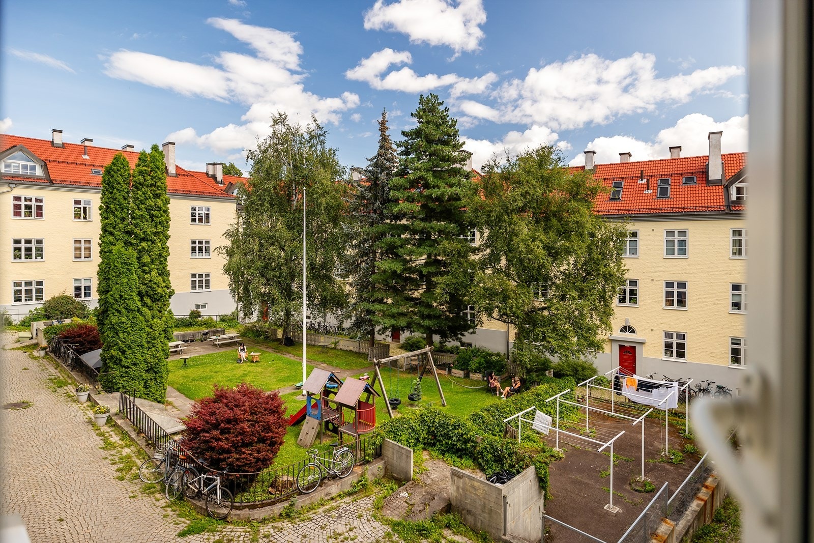 Utsikt over frodig bakgård med sitteplasser og lekeområde. Galleribilde