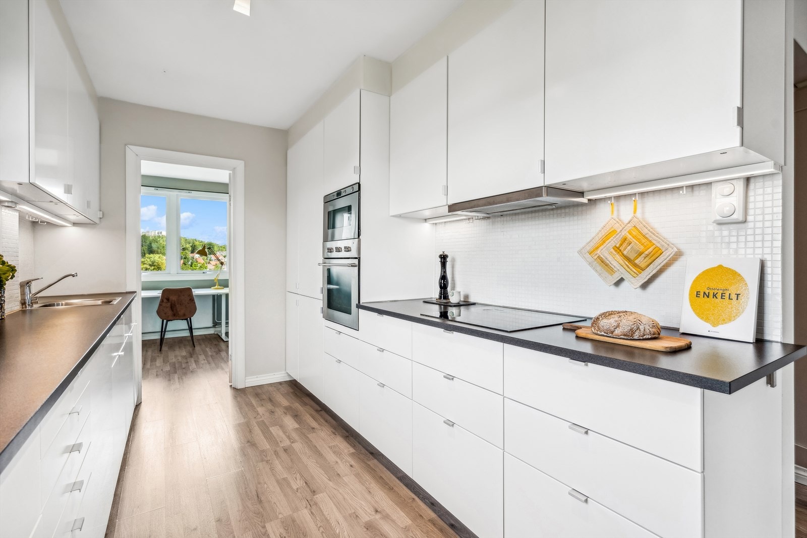 IKEA kjøkkeninnredning fra 2016. Det er en elegant enhet med mosaikkfliser over kjøkkenbenk. Innredet med hvite glatte fronter, sorte laminerte benkeplater, benkebelysning under overskap og takhøy/oppforet innredning. Galleribilde