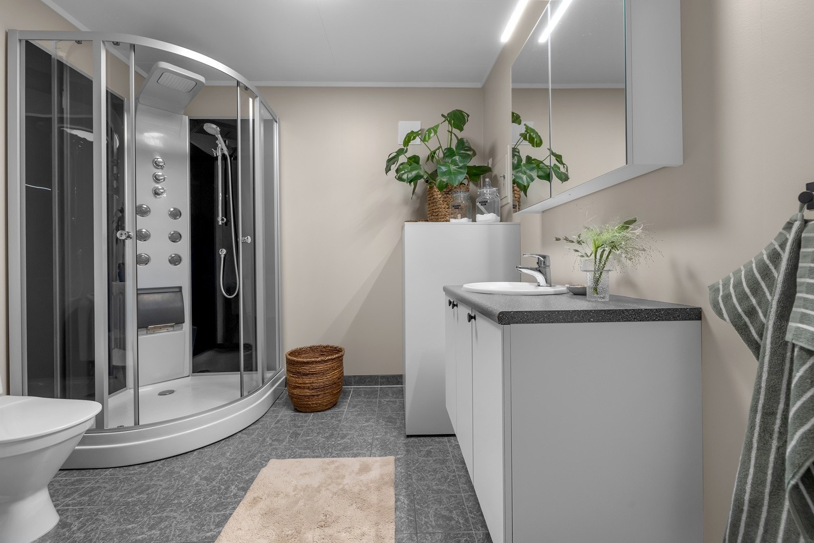 Flislagt gulv med varme, romslig dusjkabinett og innredning med god lagringsplass Galleribilde