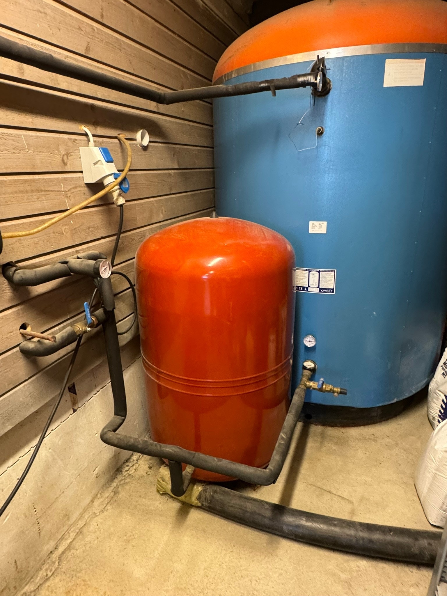 Akkumulatortanker i isolert bod i carport. Her er også luftkompressor til verksted plassert. Her vises kulvertrøret som går inn til hus, her er det bare litt rørleggerarbeid med tilkoblinger i hver ende. Galleribilde