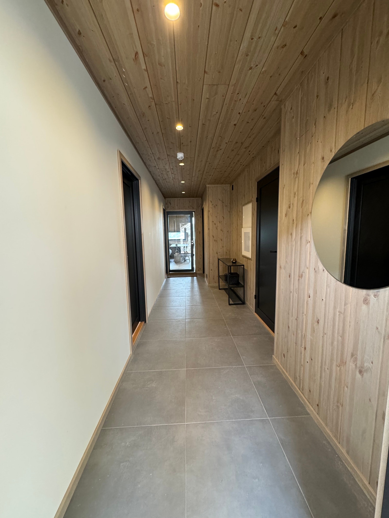 Fra gangen sett inn mot stue, noen veggpartier har limtrepanel, andre har malte lyse flater. Glass-skyvedør mellom stue og gang. Galleribilde