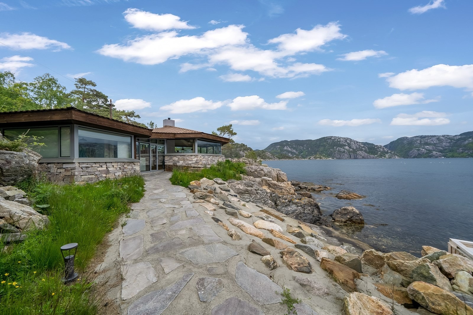 Tomta rundt hytta er pent opparbeidet med skiferbelagte heller og treterrasse blant fin naturtomt. Galleribilde